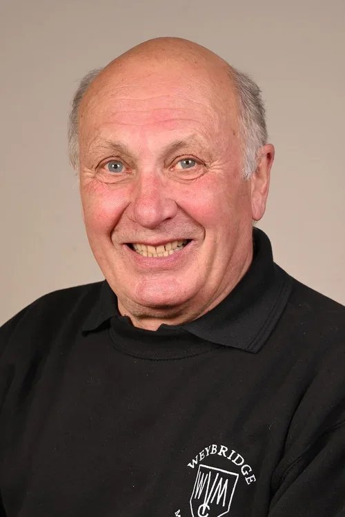 A smiling elderly man with a bald head and gray hair on the sides, wearing a black shirt with a logo that reads 'Veybridge'.