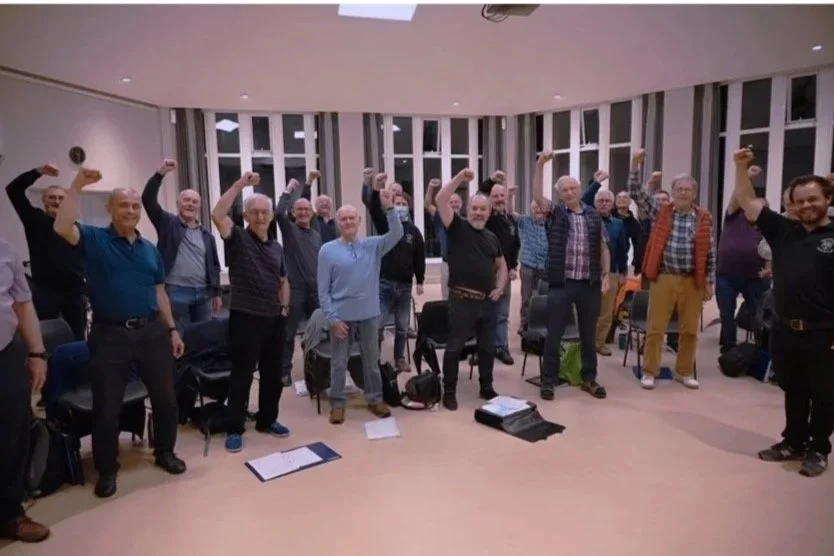 Group of people raising their fists in a room with windows and chairs.