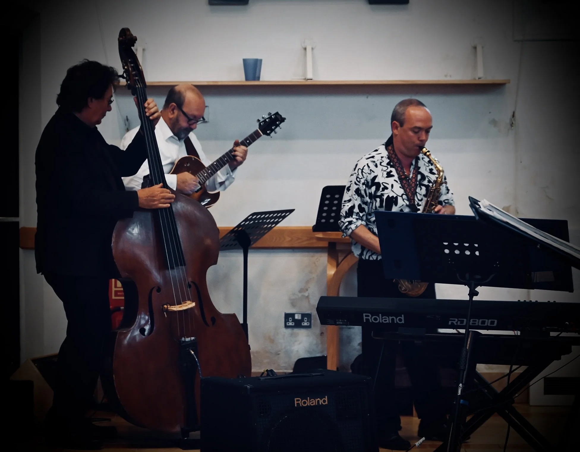 A jazz band performing indoors, featuring a double bassist, a guitarist, a saxophonist, and a keyboardist.