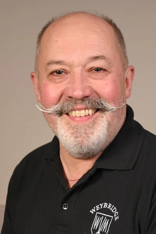 Smiling man with a beard and mustache wearing a black polo shirt with a Weybridge logo.