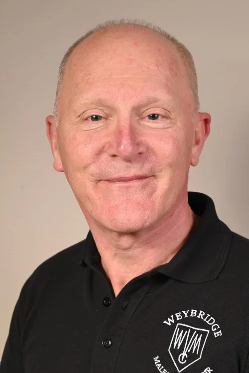 Portrait of a smiling middle-aged man with short light-colored hair, wearing a black polo shirt with a logo that reads 'Weybridge.'