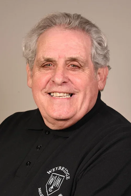 An older man with gray hair smiling, wearing a black polo shirt with a logo that says 'Weybridge'.