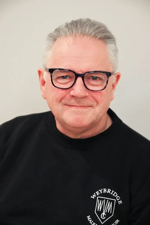 A middle-aged man with gray hair, wearing black glasses, smiling, and dressed in a black Wewbridge T-shirt.
