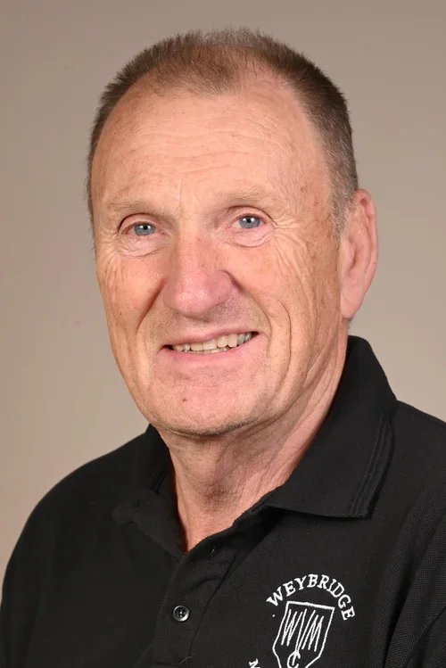 A middle-aged man with light skin, short light brown hair, and blue eyes, smiling slightly, wearing a black polo shirt with the Weyerbridge logo on it.