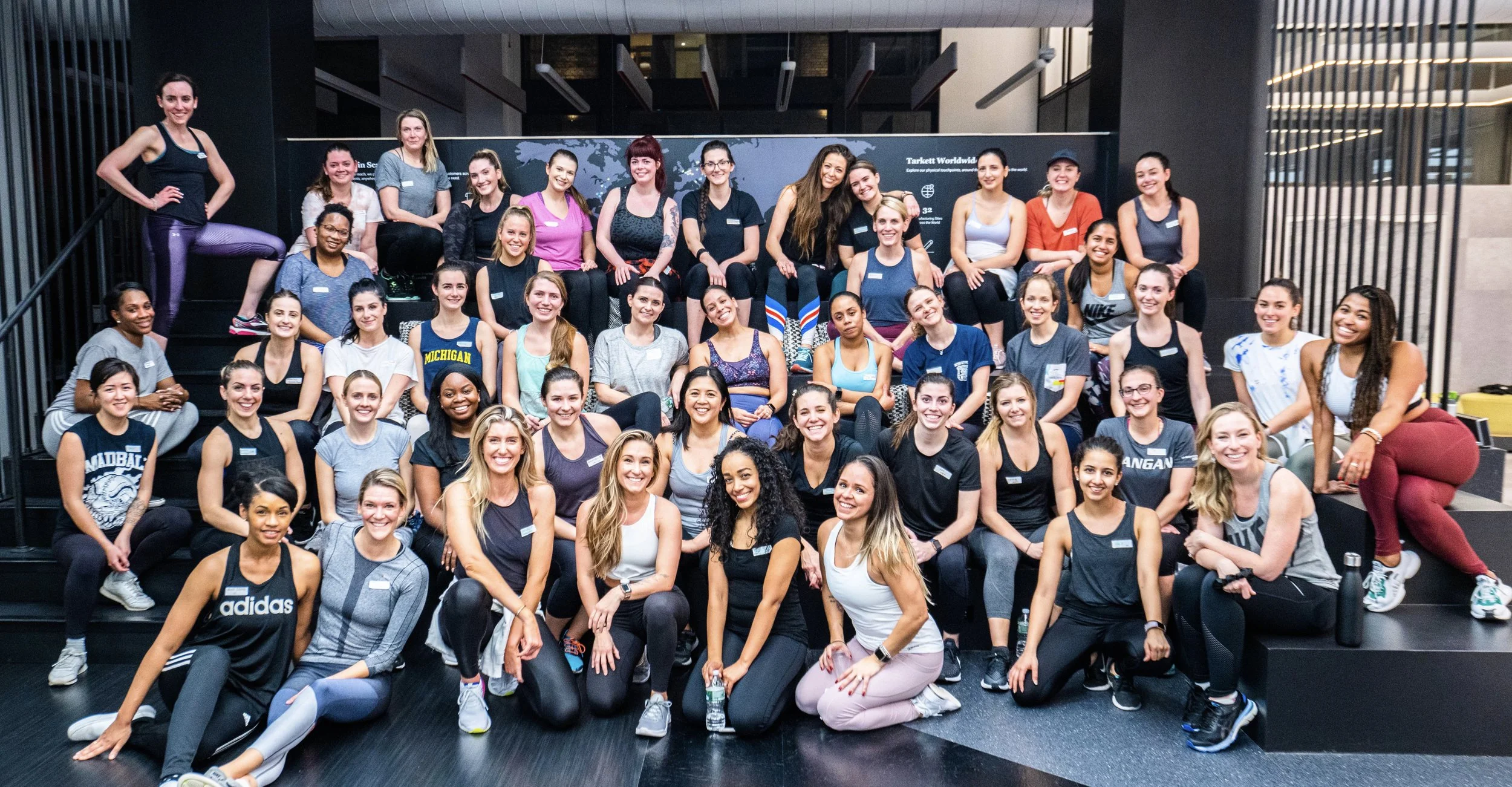 Group photo of 37 women, some in workout clothes, posing on stairs and floor indoors.
