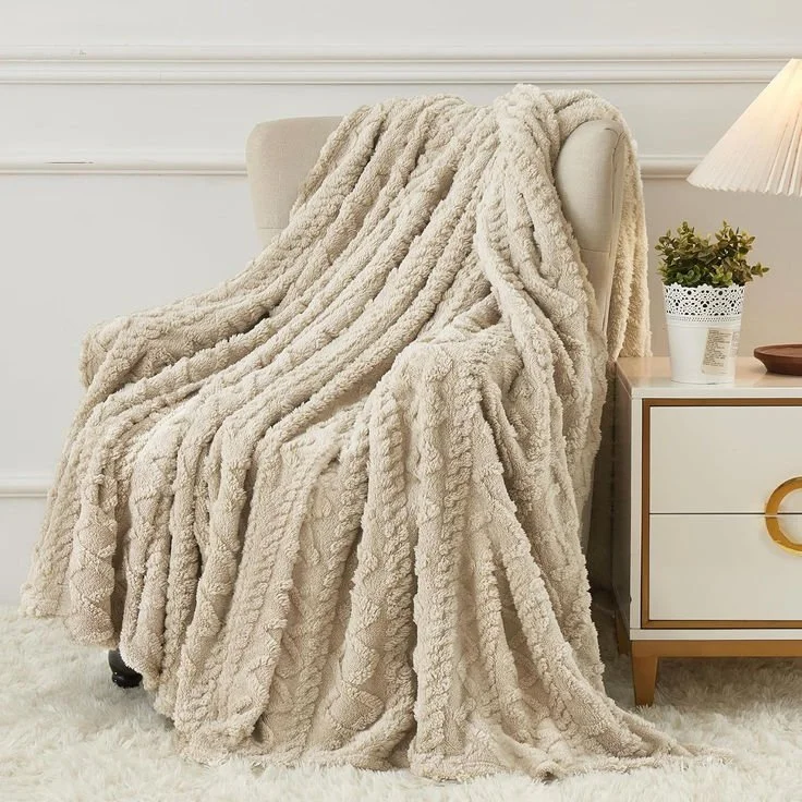 Cream-colored plush blanket draped over a beige armchair in a cozy living room with a side table holding a potted plant and a table lamp.