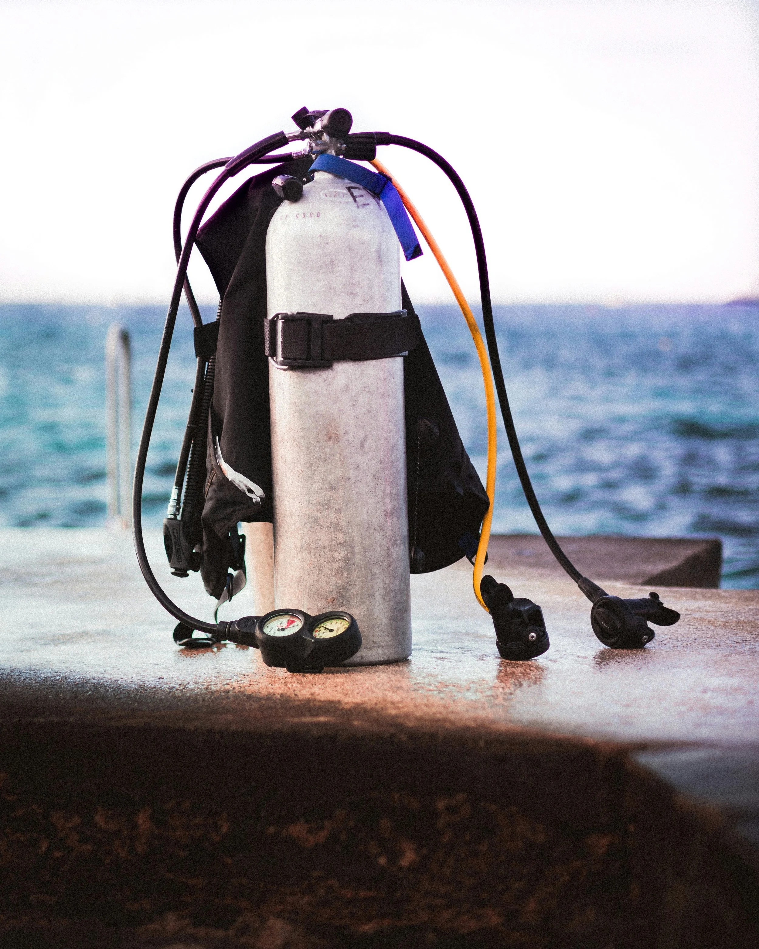 Scuba diving equipment including an oxygen tank, regulator, and gauges on a dock near water.