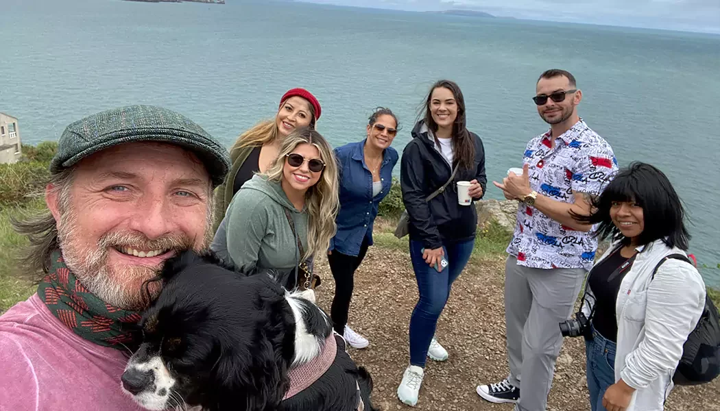 Group of seven people and a dog standing on a cliff overlooking the ocean, smiling for a photo.