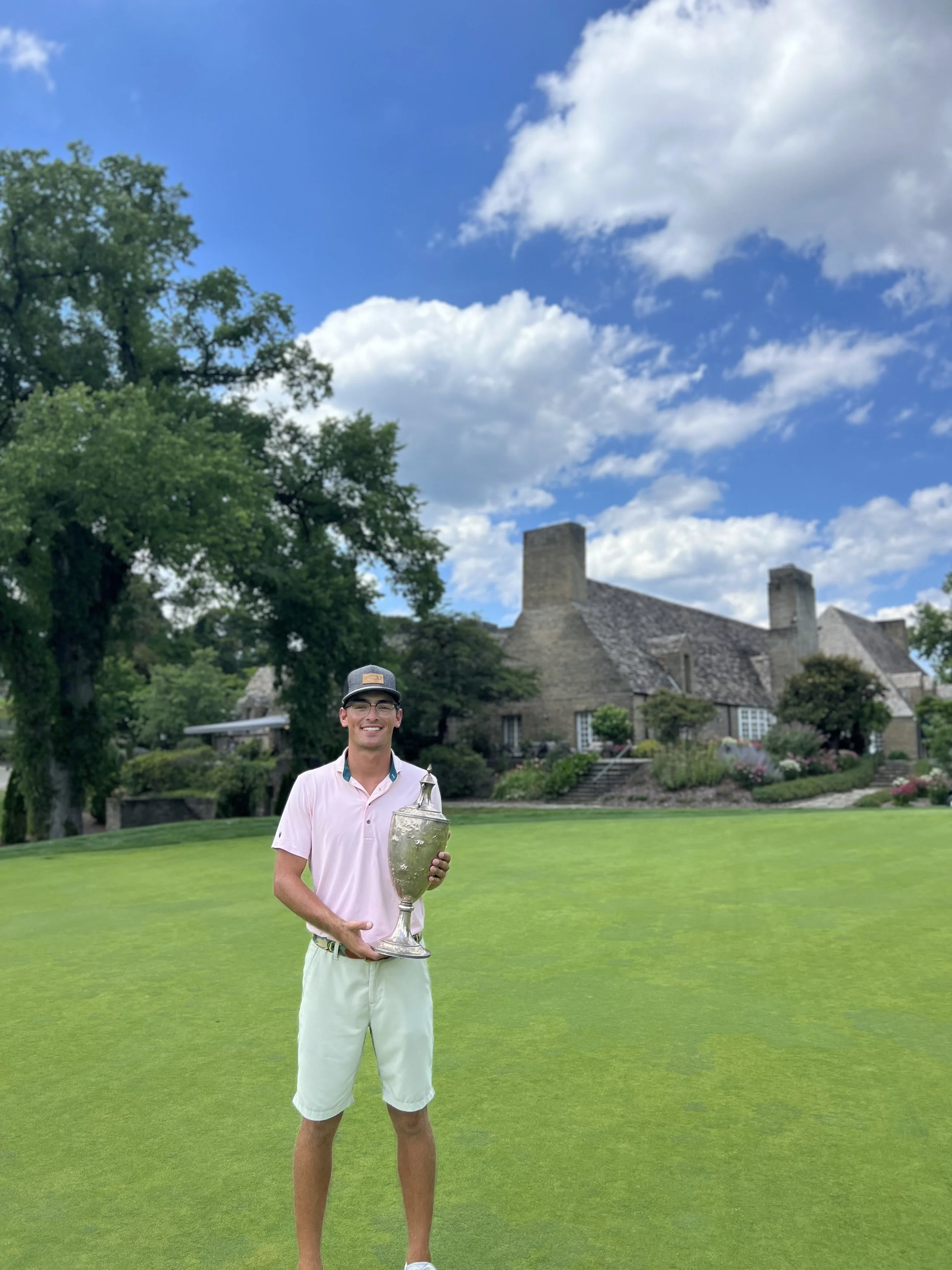 Golf performance coach Amani D'Ambrosio holding championship trophy at elite golf course clubhouse after tournament victory, demonstrating competitive golf experience and credibility