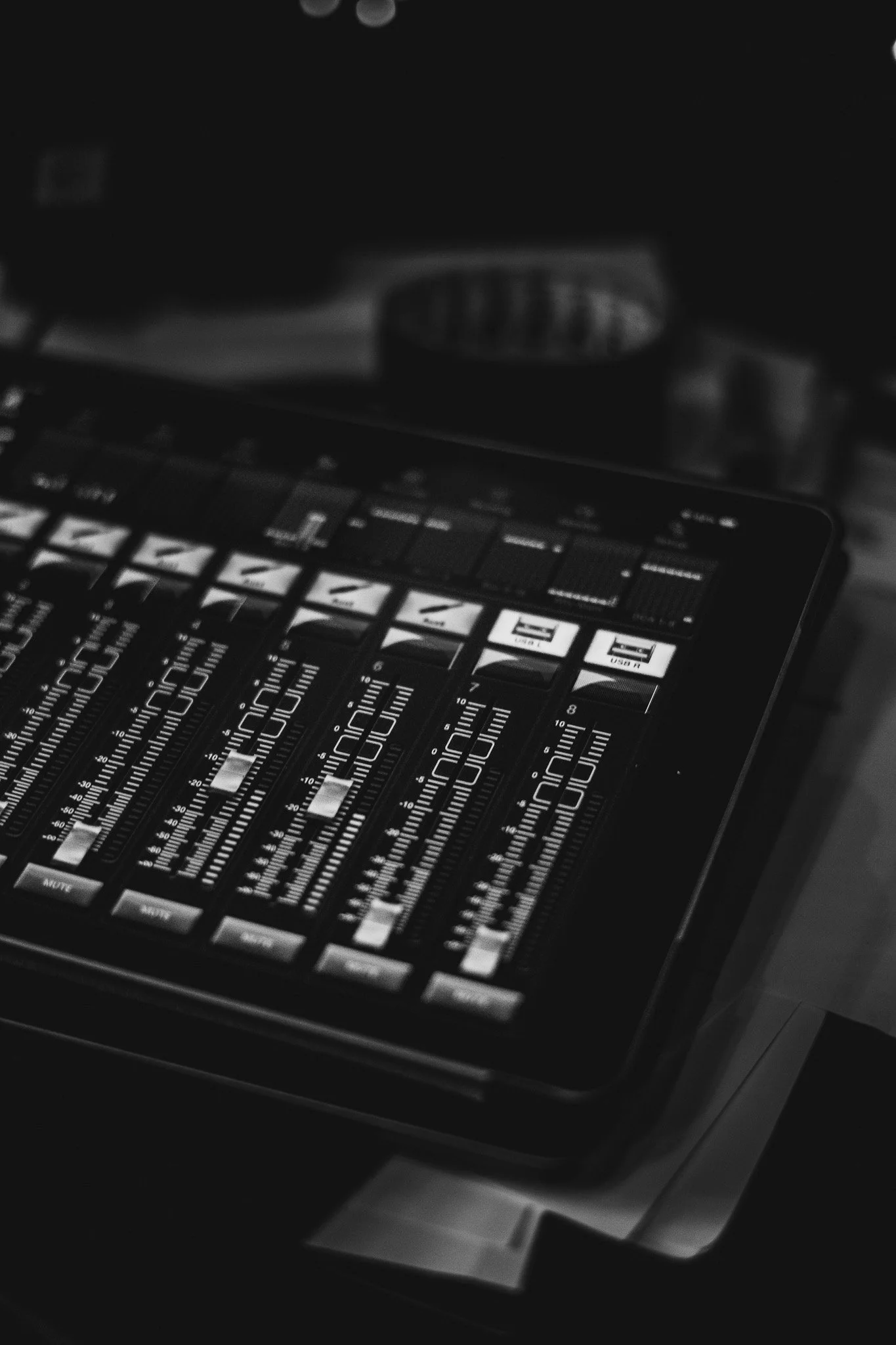 A digital audio mixer with multiple sliders and controls, black and white photo.
