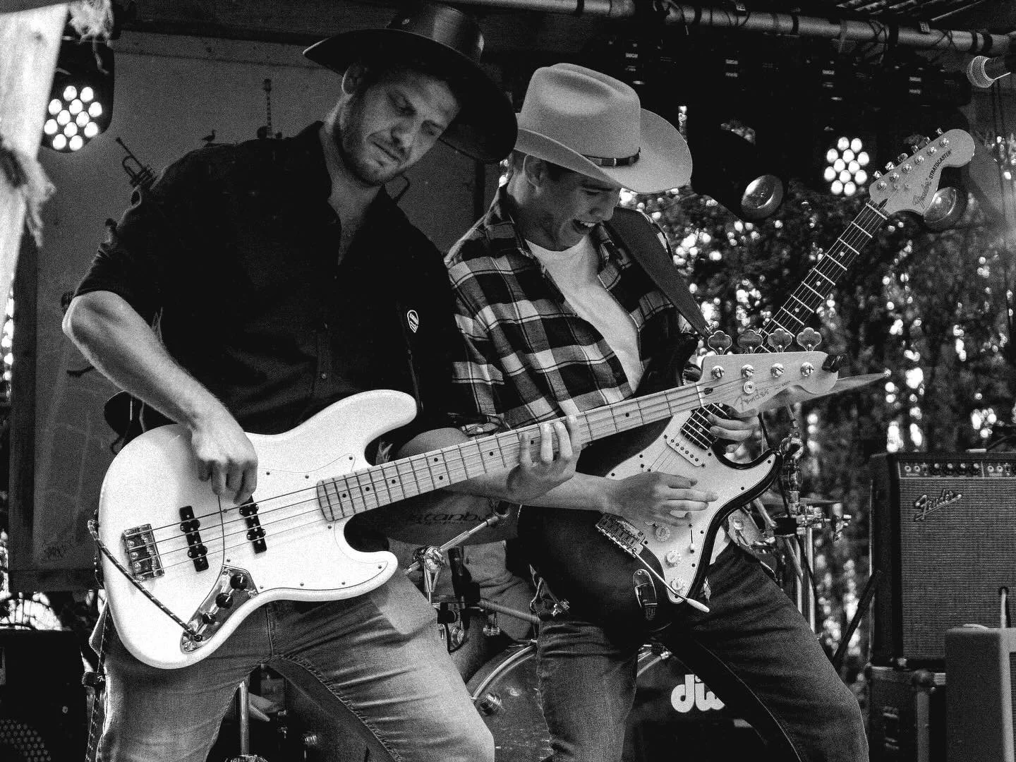 Two musicians playing electric guitars on stage during a live performance, with stage lights and equipment visible.