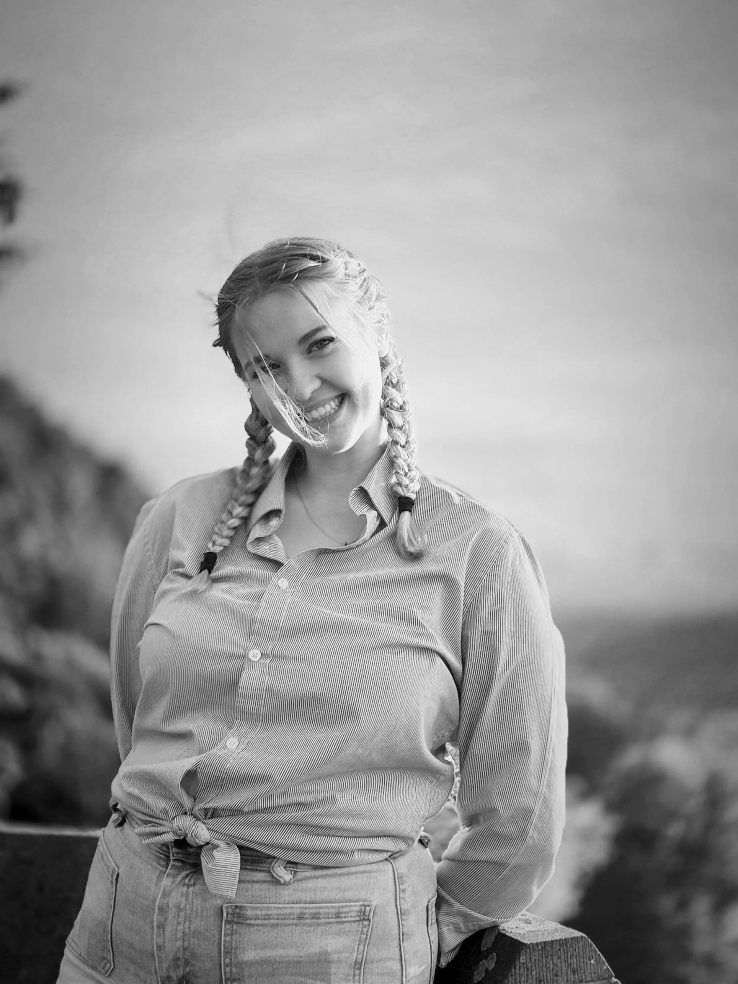 A young smiling woman with braids outdoors near a body of water.