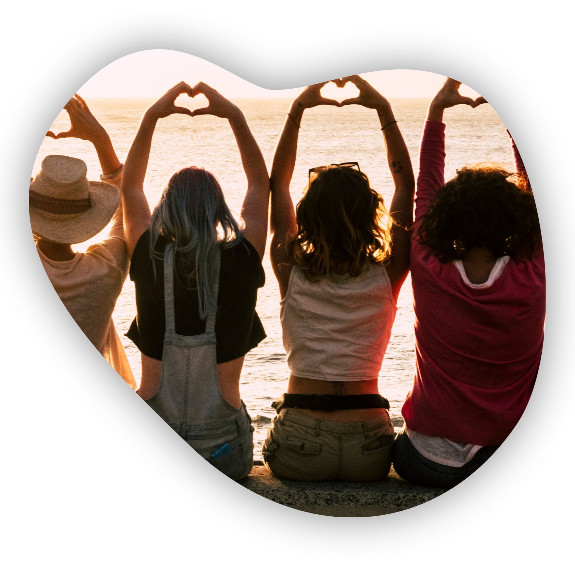 Four friends sitting by the water at sunset, making heart shapes with their hands.