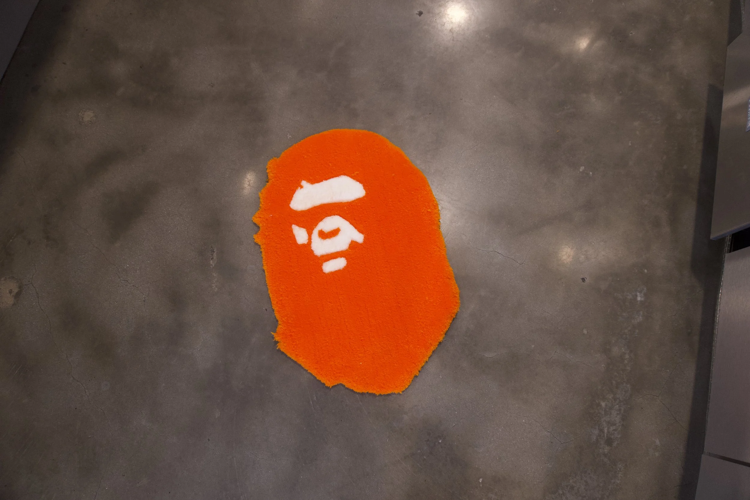 Orange rug with white design resembling a face on a concrete floor.