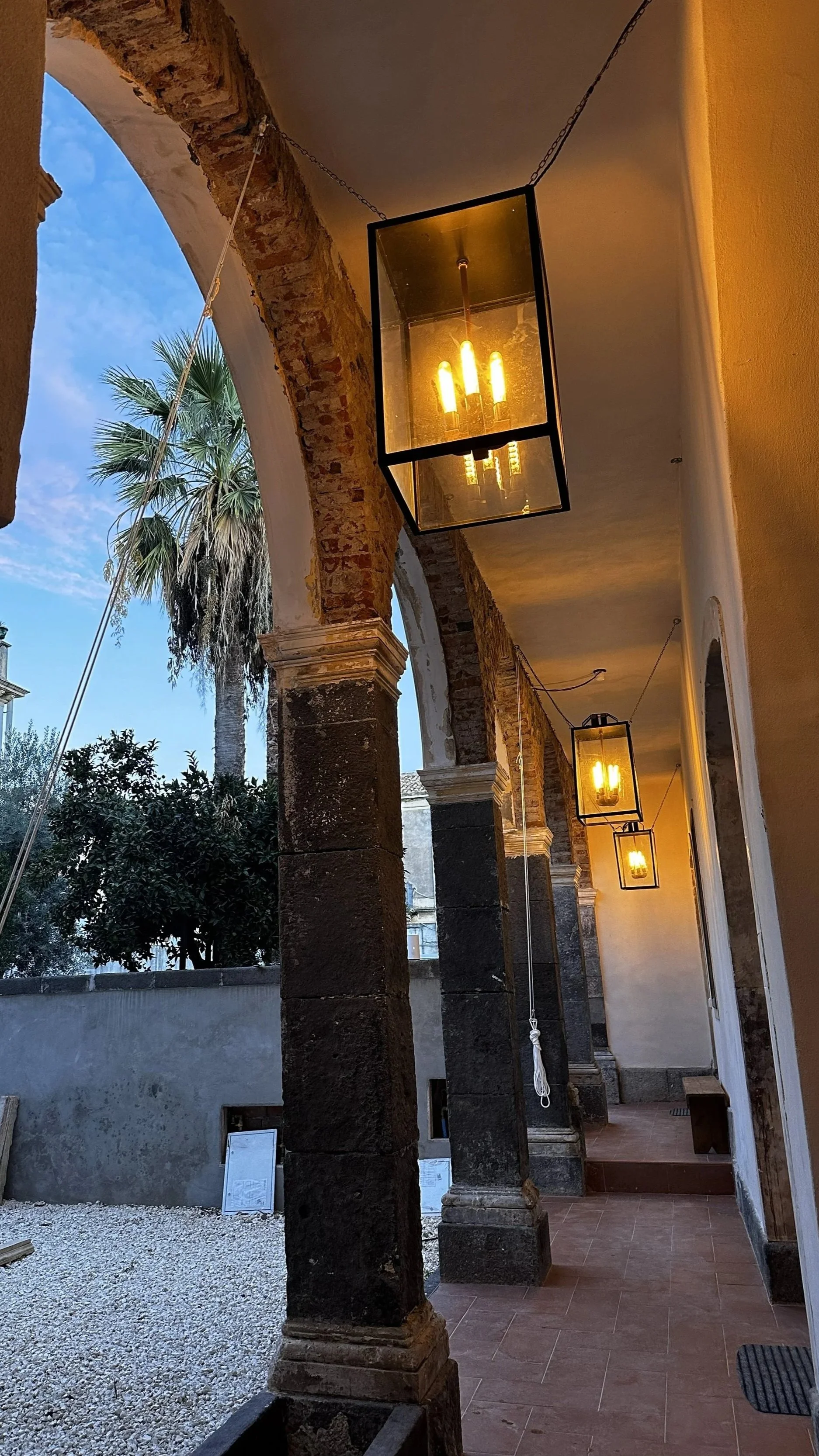 Exterior corridor with brick arches, hanging lanterns, and a view of palm trees and sky