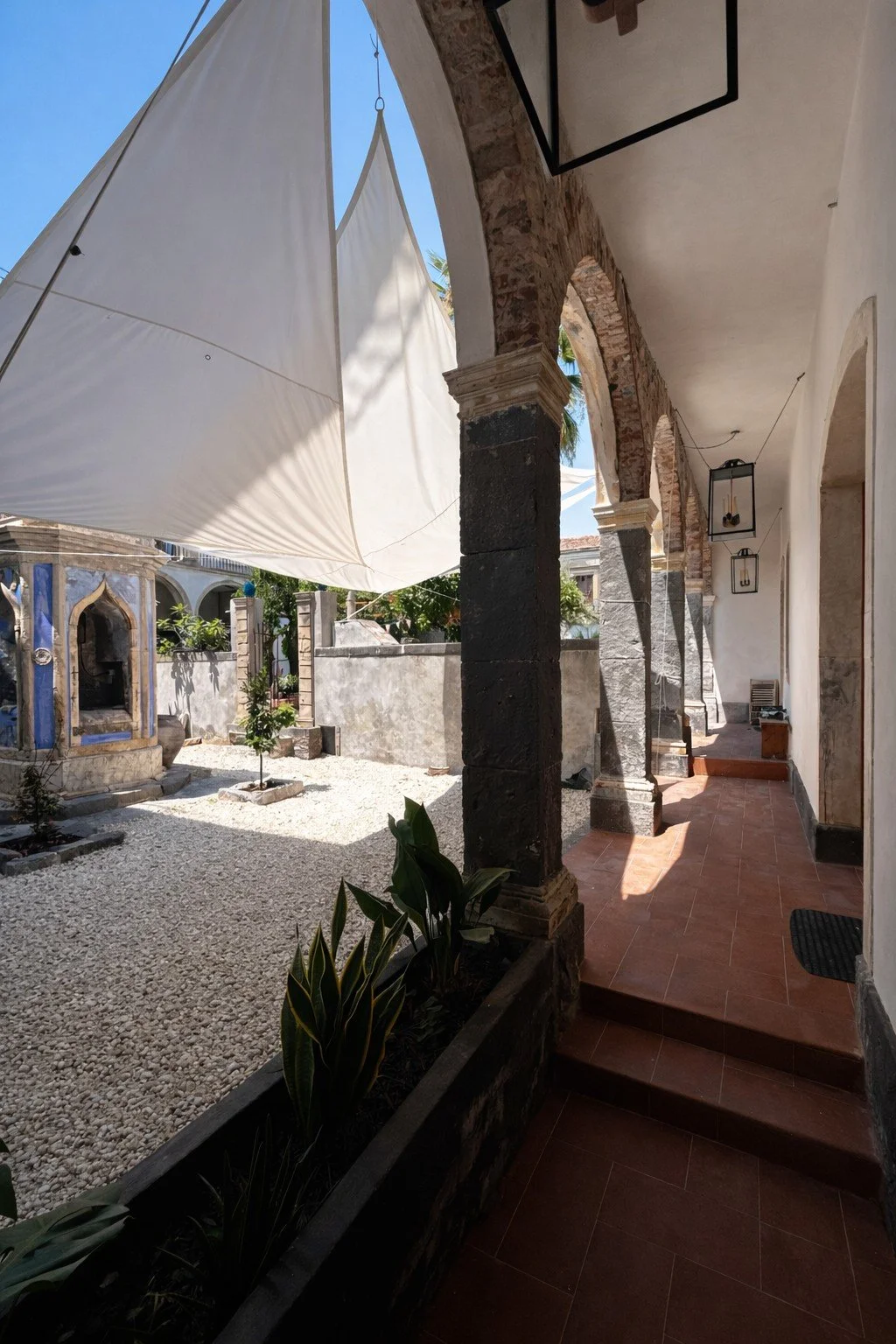 Shaded patio walkway with stone columns and lantern lights at Tacasa courtyard.