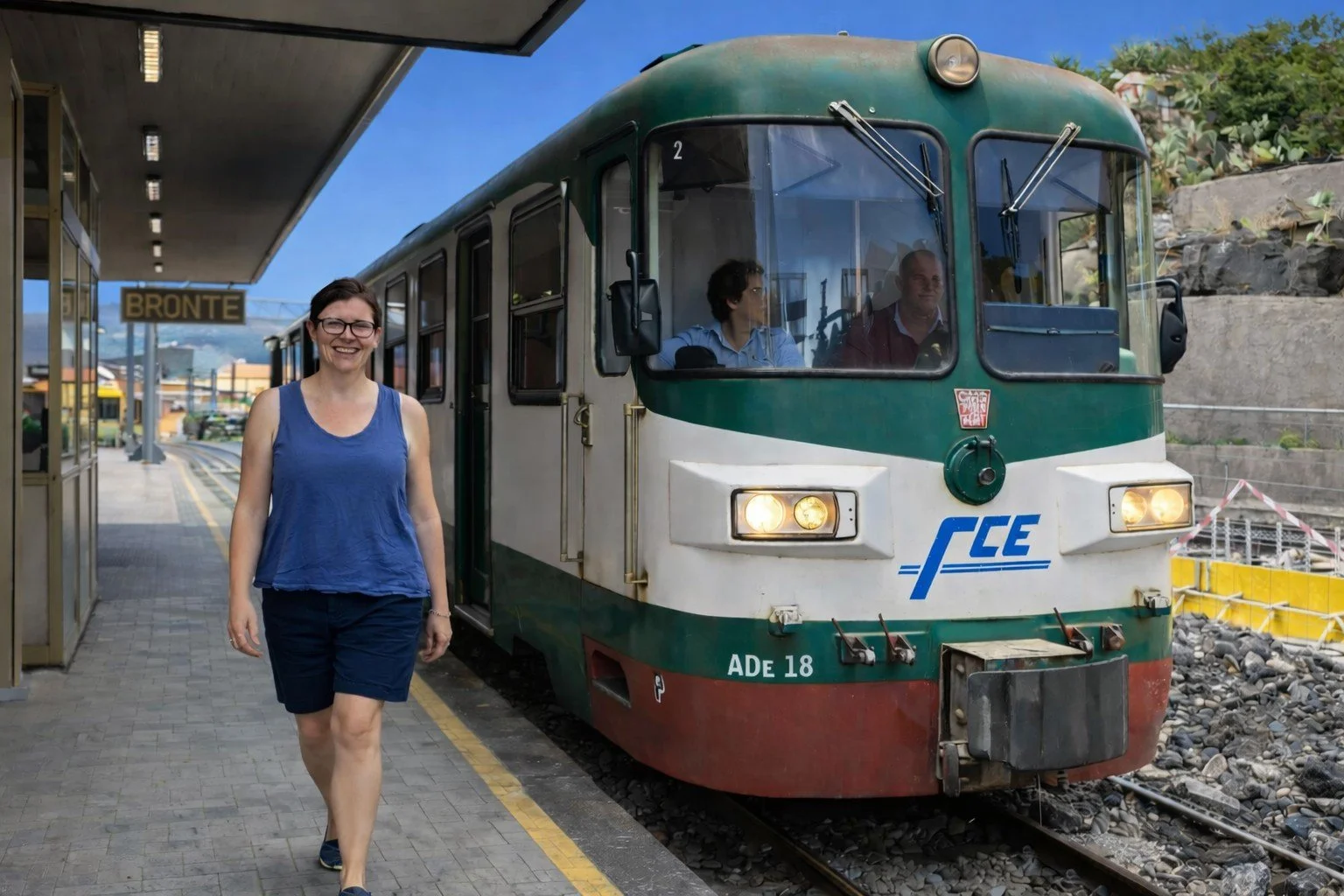 Woman smiling on a train platform next to a green and white train.
