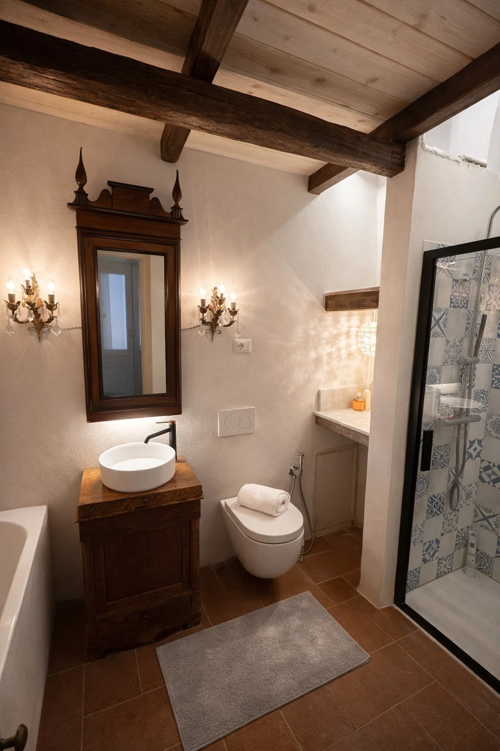 A rustic bathroom with a wooden ceiling and beams, a mirror with a wooden frame, vintage wall sconces, a modern toilet with a rolled towel, a small sink on a wooden cabinet, and a walk-in shower with patterned tiles.