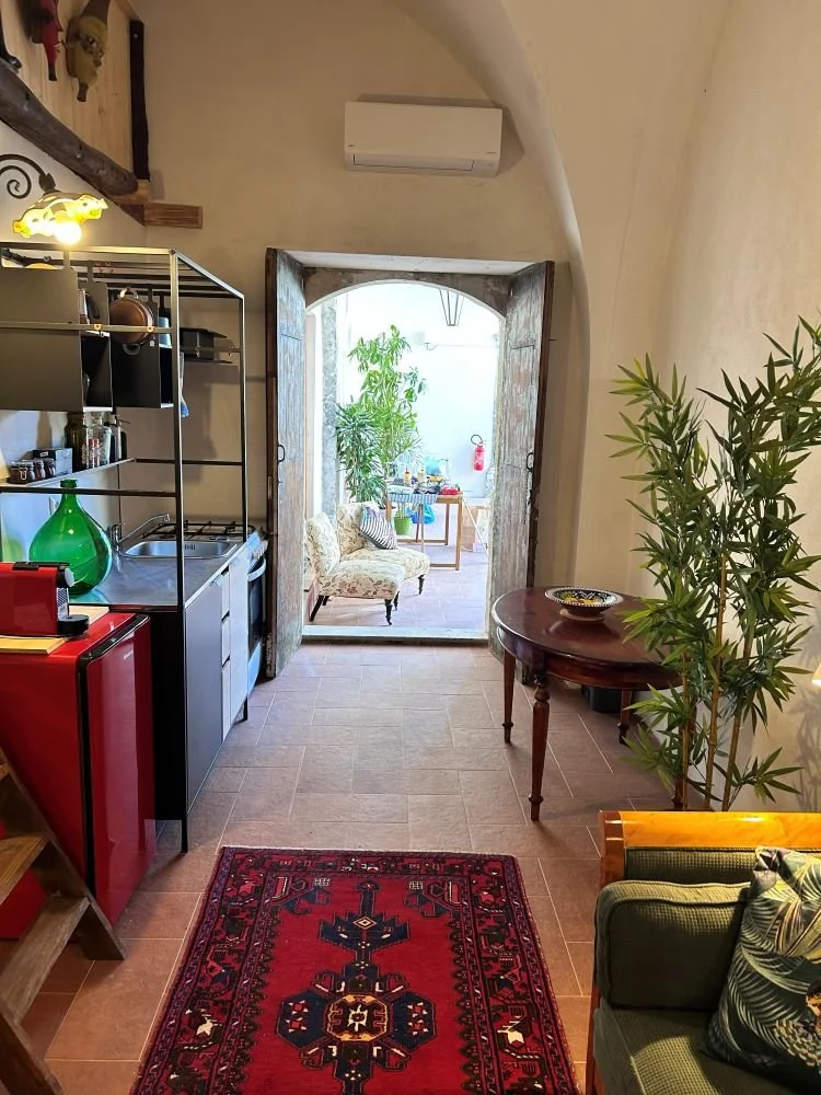 Compact kitchen setup with black metal frame, open shelves, beige and black cabinets, a stainless steel sink, a white stove, and a red mini refrigerator. Walls are white, and there is a decorative ceiling light.