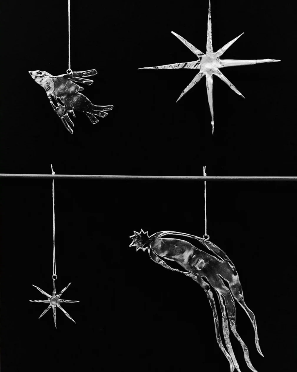 Decorazioni natalizie in vetro trasparente di vari forme come stella, pesce, calamaro e animale, appese a fili con sfondo nero.