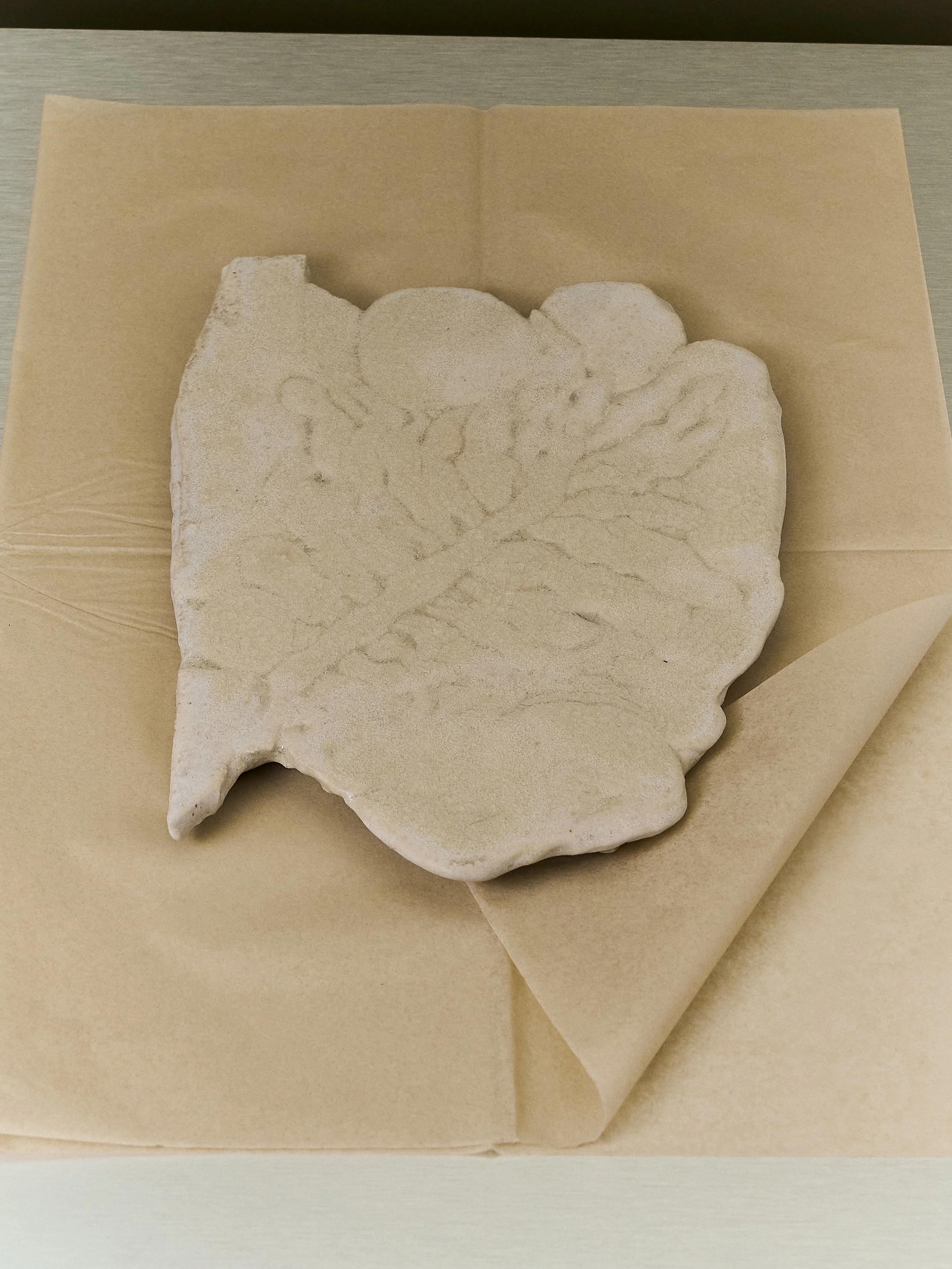 Piastrella di pietra con impronte di foglie, posizionata su carta da forno o simile.