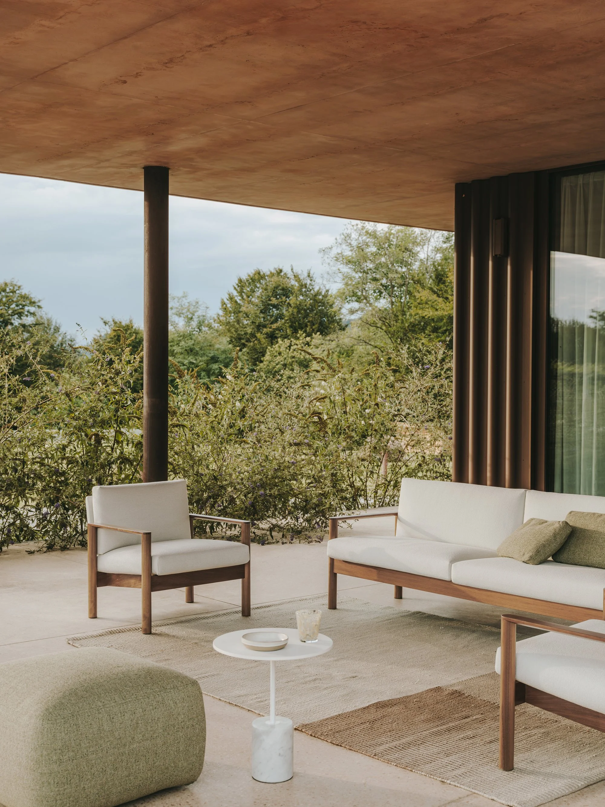 Balcone con mobili in legno e tessuto, vista su vegetazione verde, pareti nere e soffitto in muratura