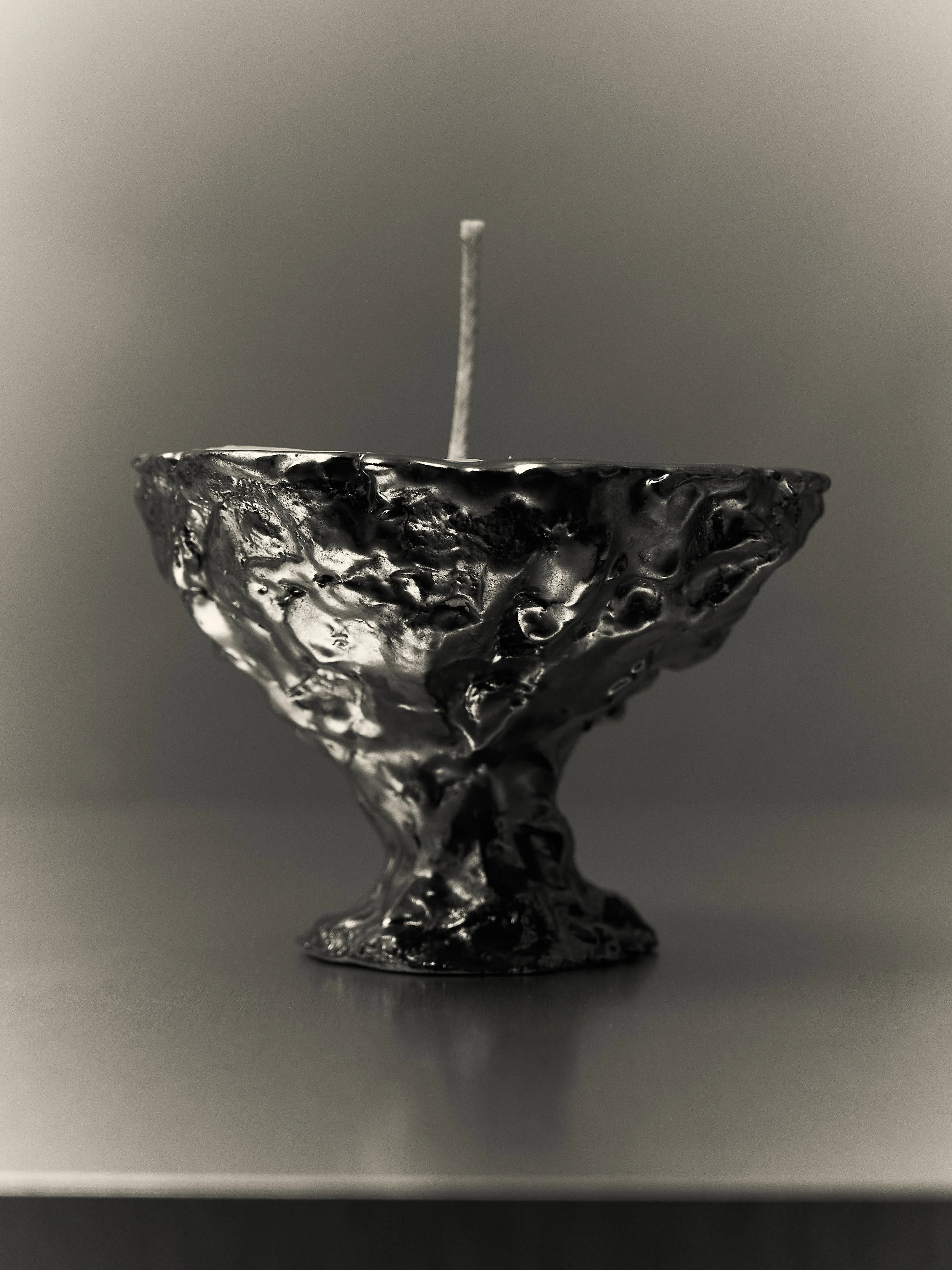 Candela nera in metallo con superficie irregolare, con uno stoppino bianco al centro.