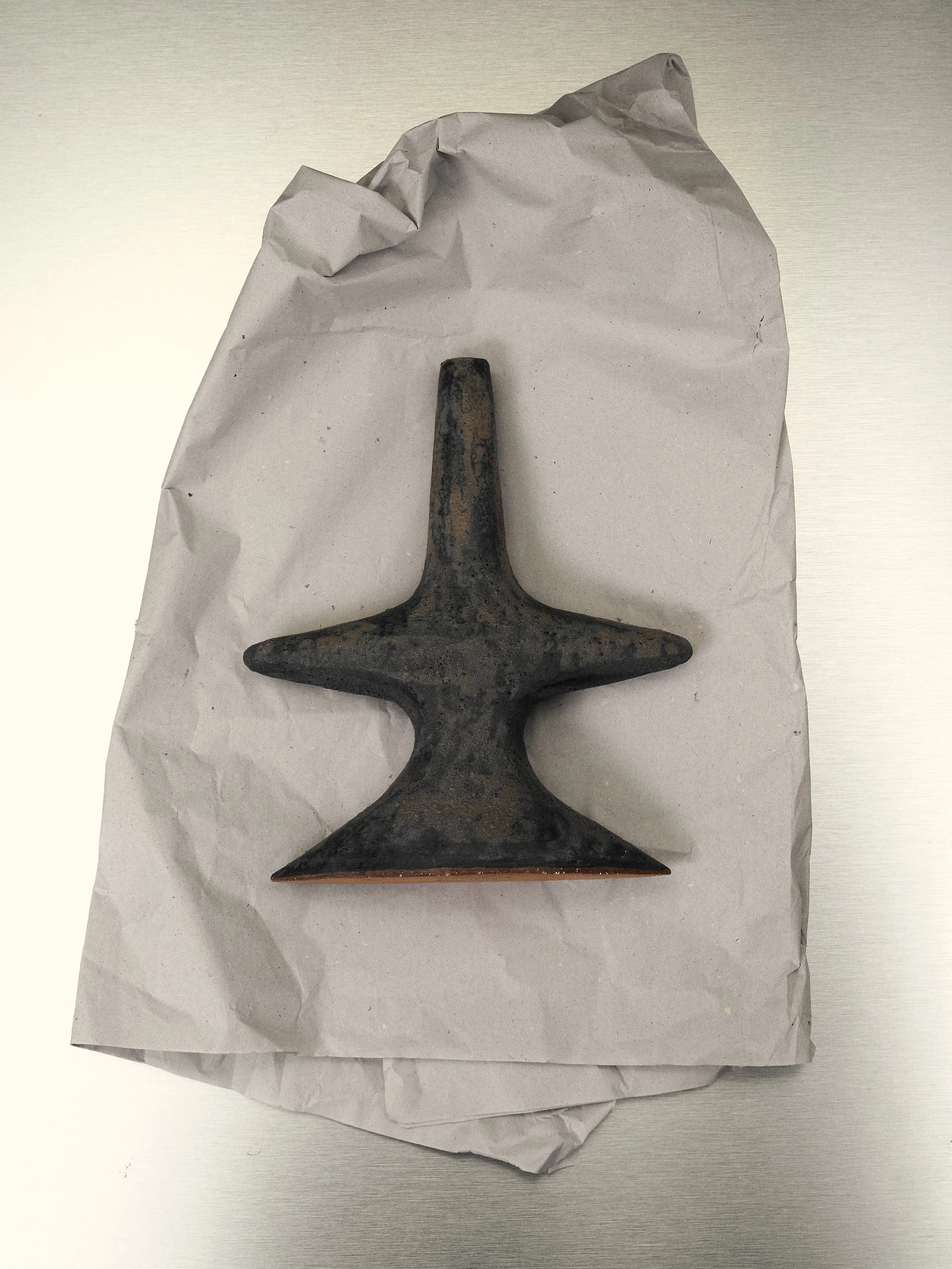 Un cusp ingranato con tre punte, probabilmente un chiodo o un attrezzo di ferro, appoggiato su carta bianca.