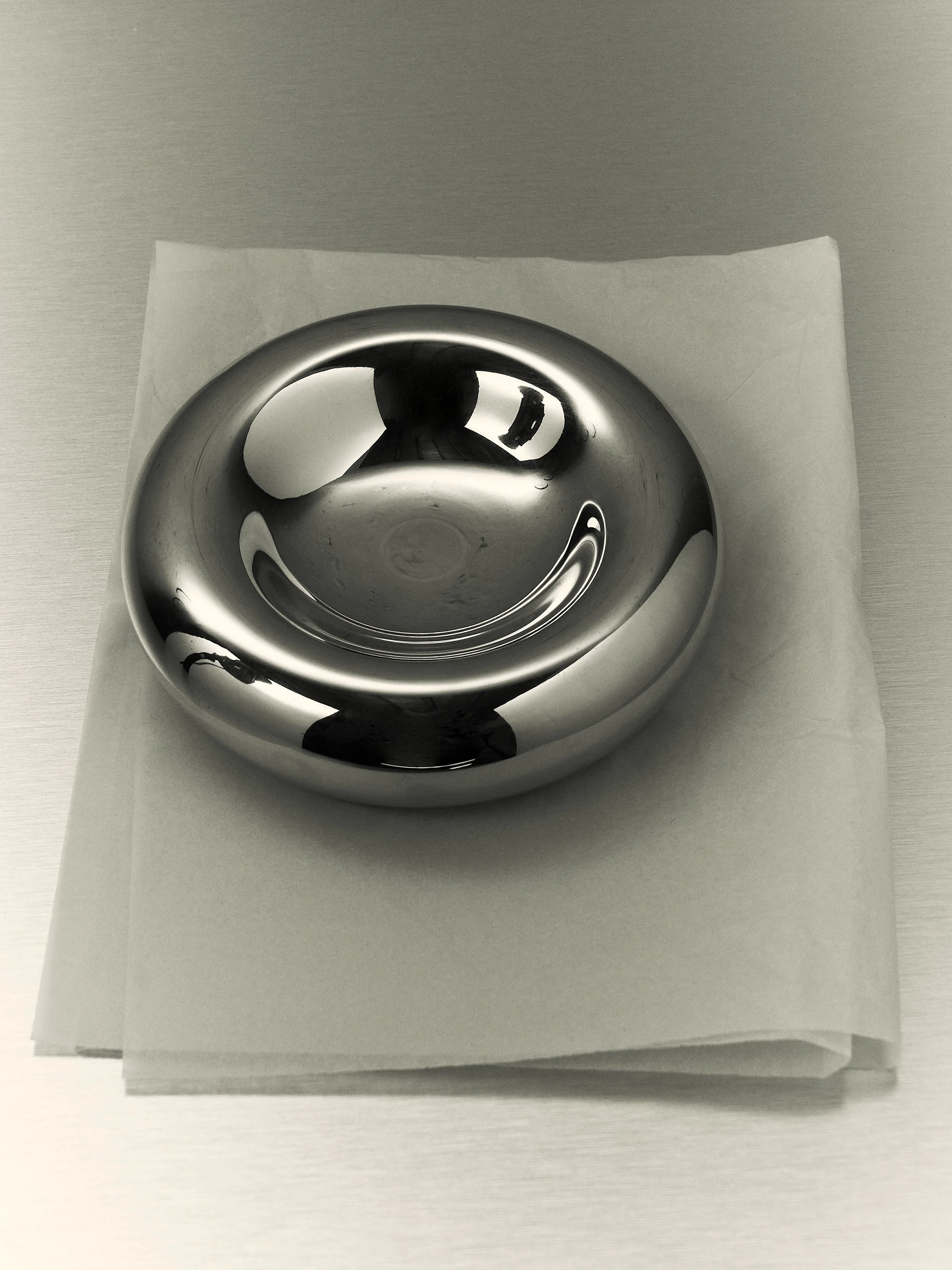 Una ciotola di metallo, lucida e riflettente, poggiata su un tovagliolo bianco su una superficie