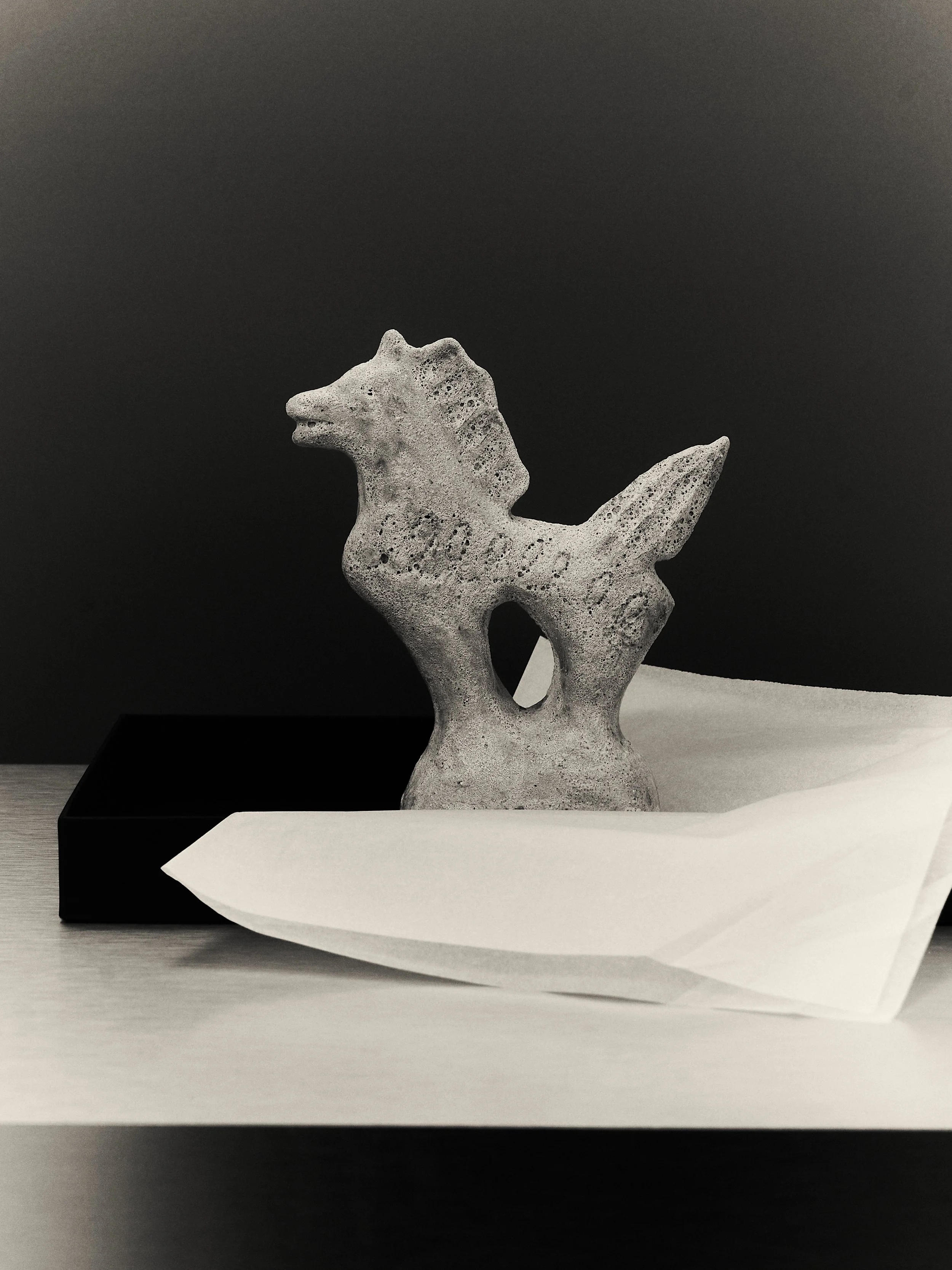 Statua di un cavallo futuristica in pietra su un tavolo, con carta bianca e scatola nera sullo sfondo.