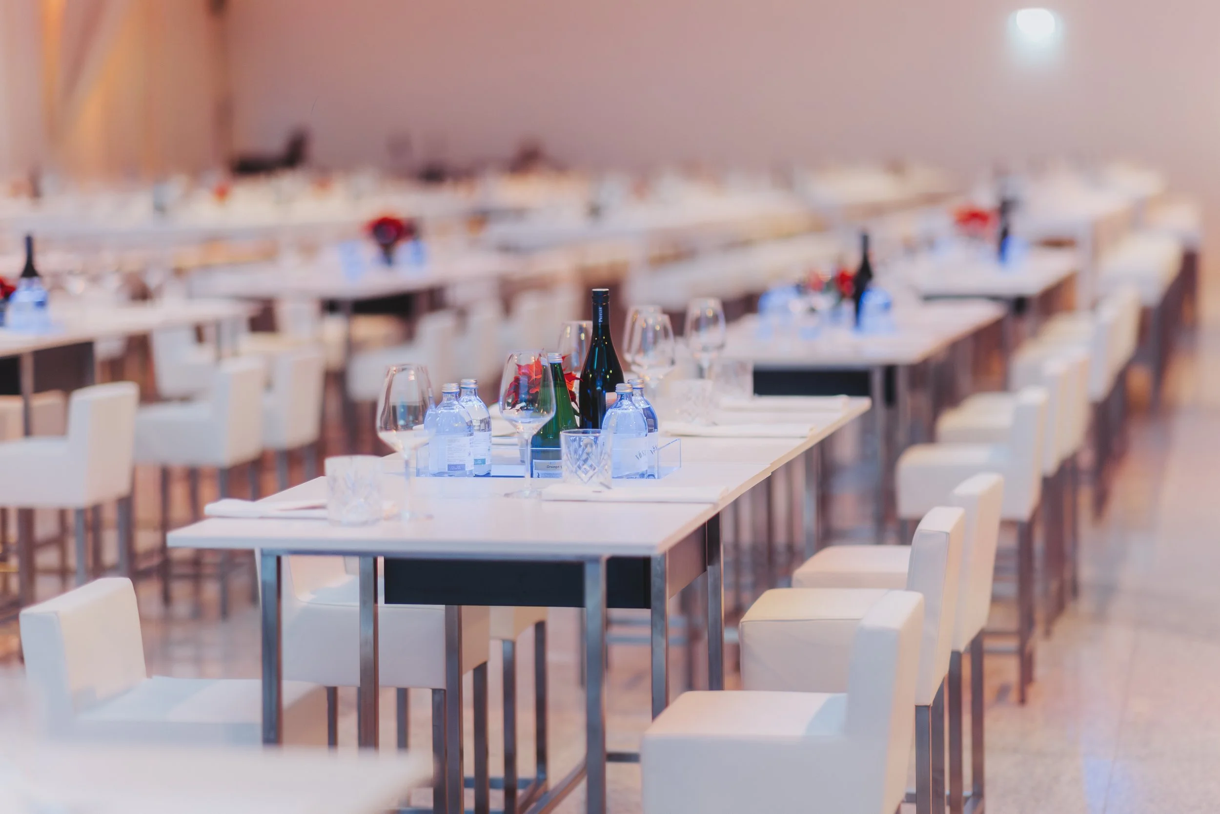 Leere festliche Tafel in einem großen Saal, gedeckt mit Wein, Wasserflaschen, Gläsern und Plätzen, für eine Veranstaltung oder Feier vorbereitet.