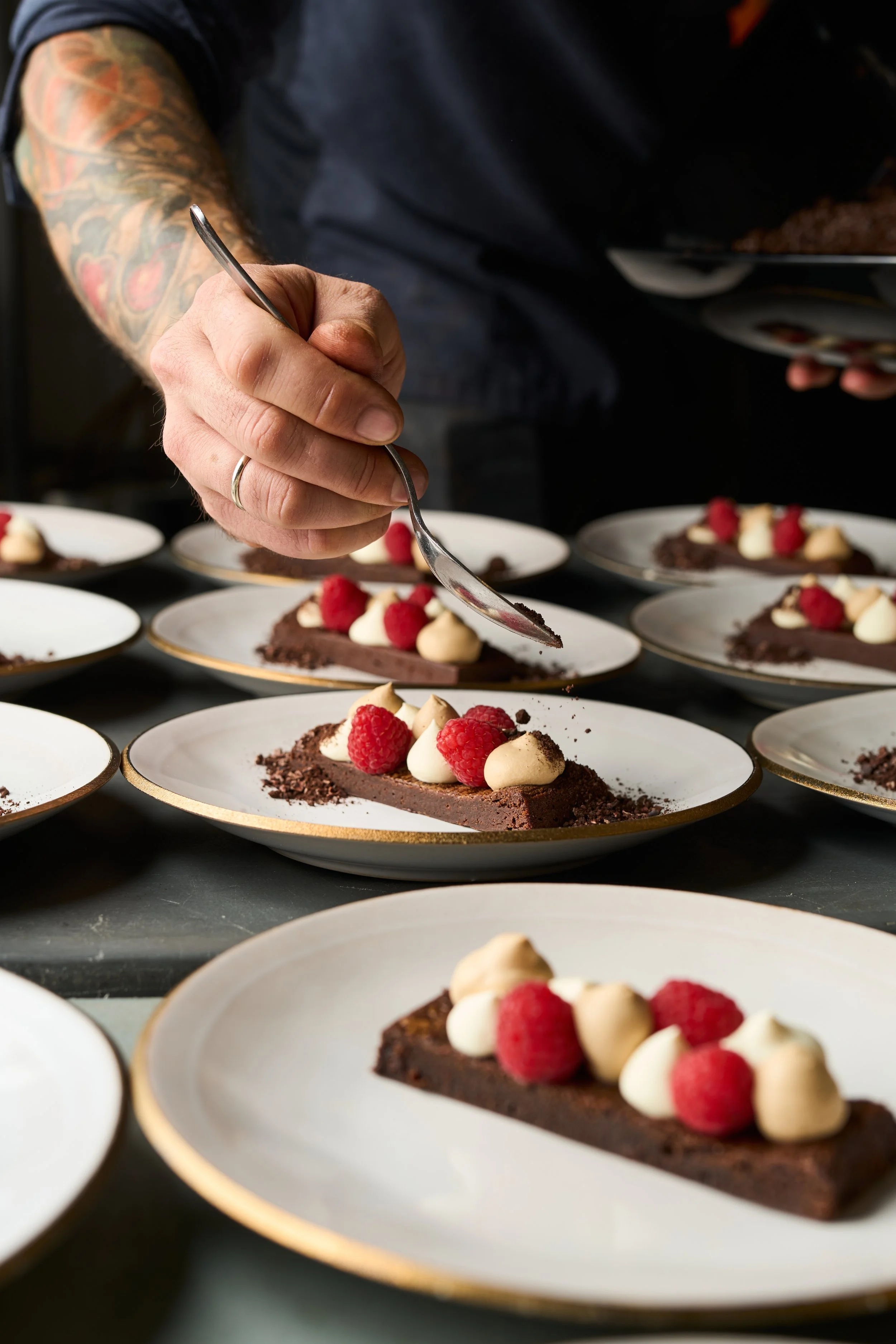 Ein Koch dekoriert Schokoladentarte auf weißen Tellern mit Himbeeren und weißen Cremakügelchen.