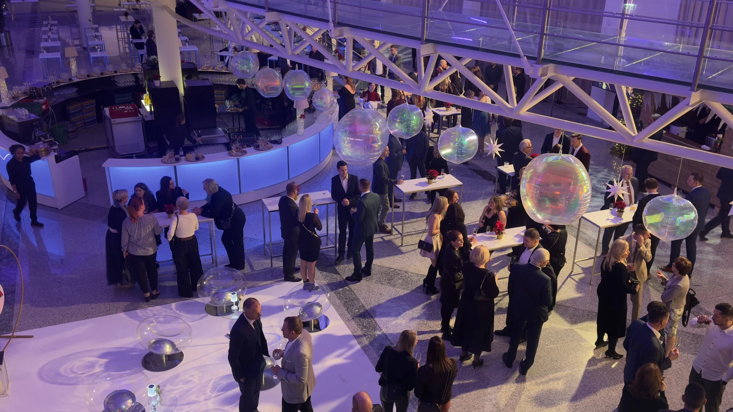 Bilder von einer festlichen Veranstaltung mit Menschen, die an Tischen und Stehtischen im Raum stehen, dekoriert mit Weihnachts- und Silvesterelementen, mit einem festlich beleuchteten, modernen Interieur.