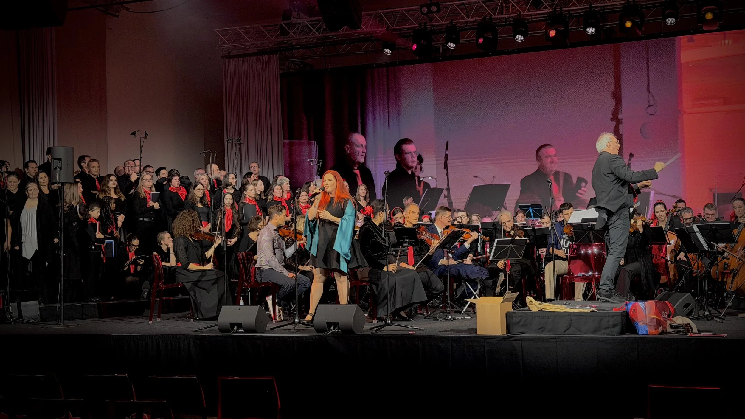 Ein Orchester mit Dirigentin und Sängerin auf einer Bühne während eines Konzerts.