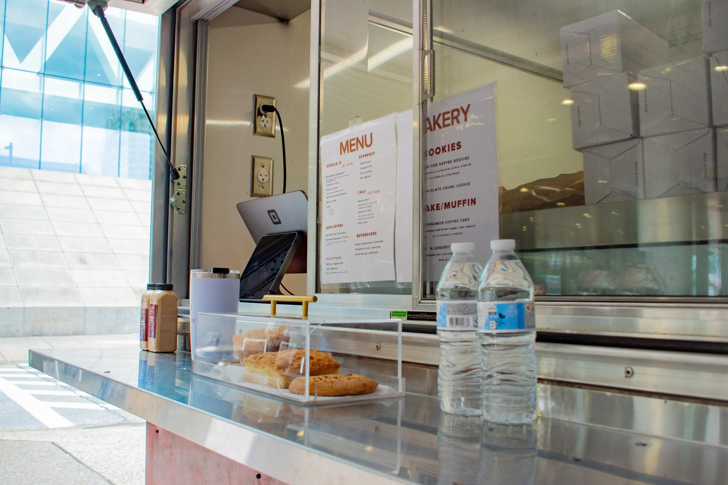 Food truck serving cookies, with two bottled waters, condiments, and a display case of cookies on the counter.