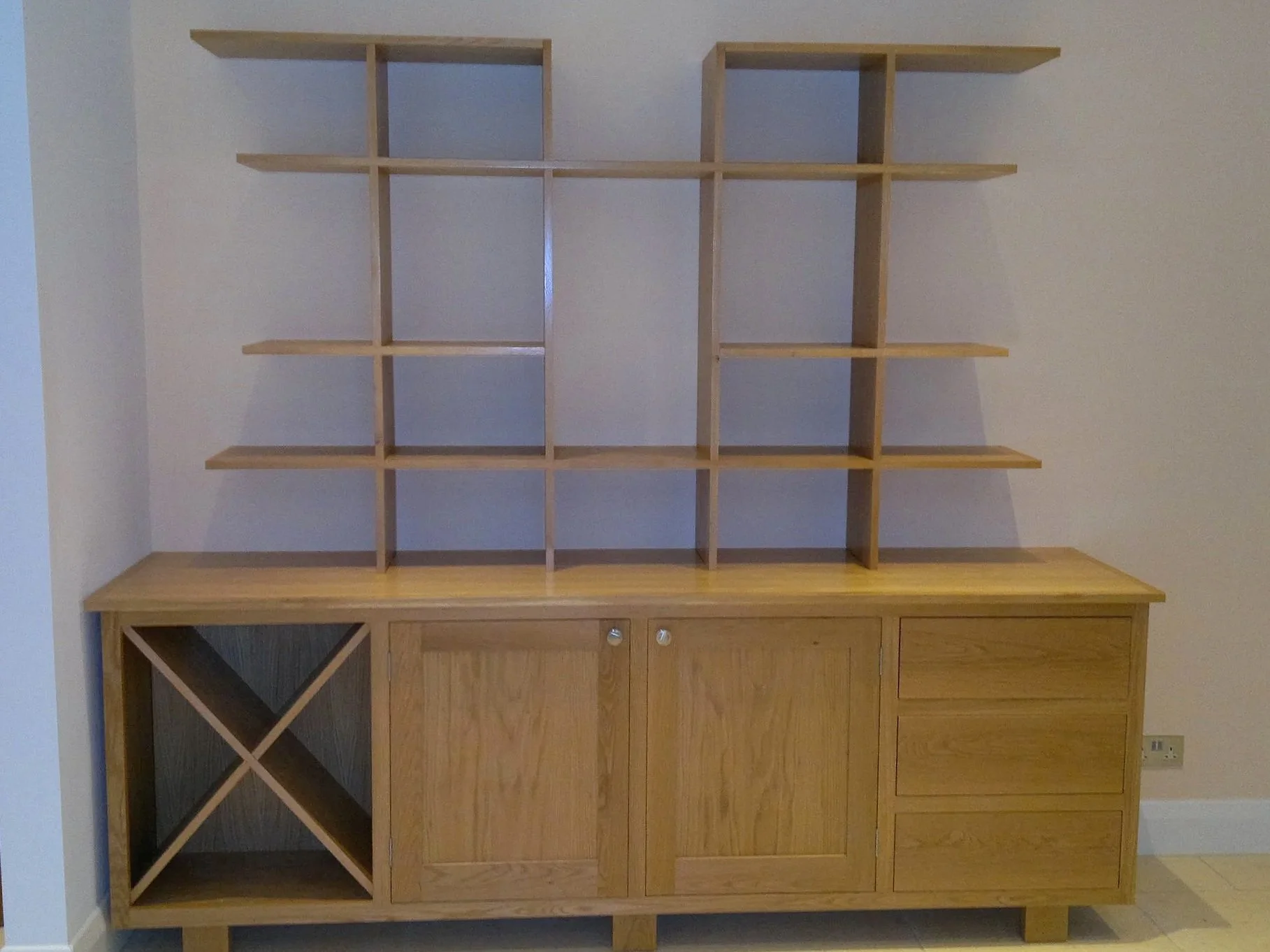 Wooden sideboard with open shelves and drawers, placed against a light-colored wall.