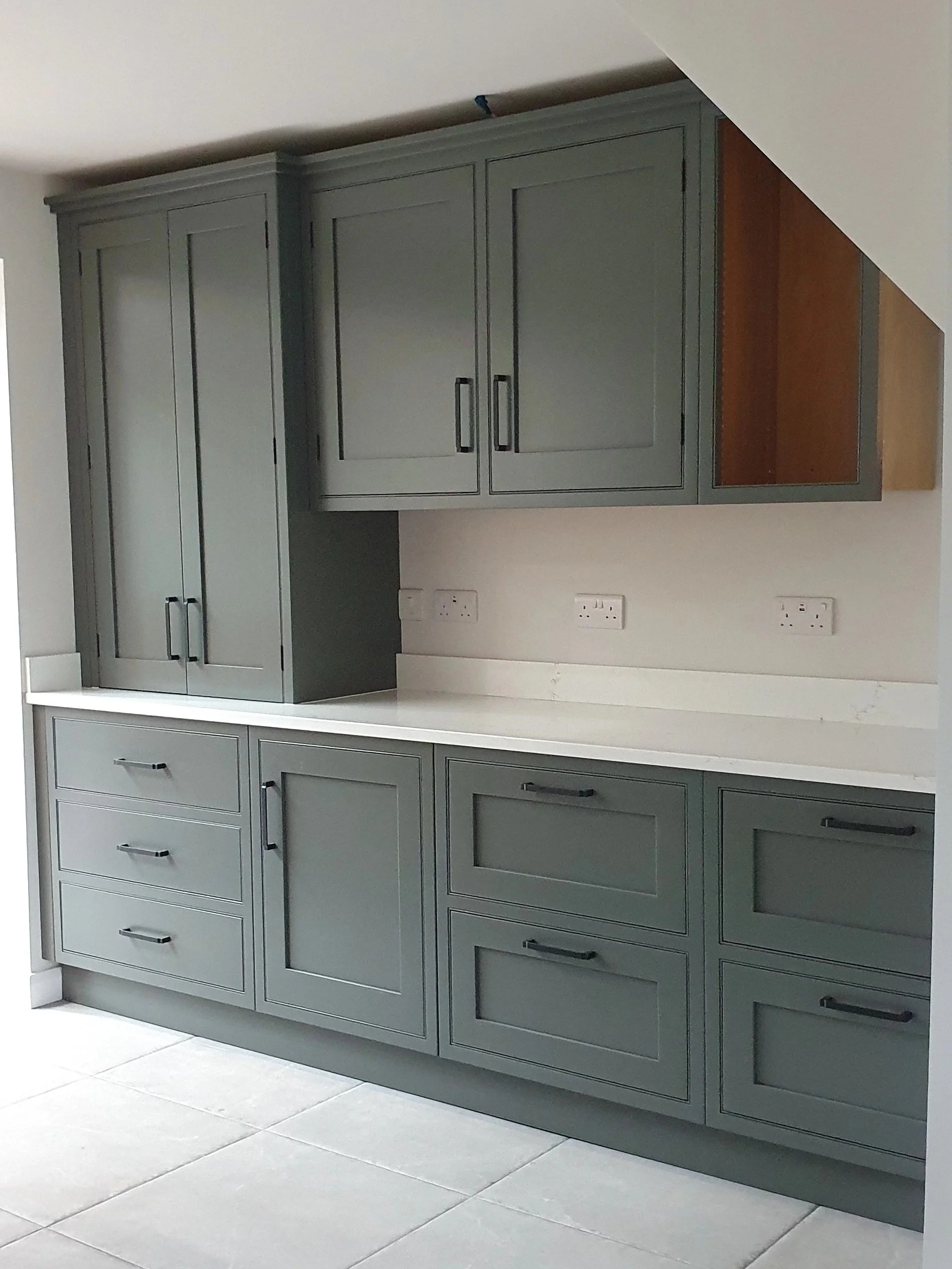Modern dark grey kitchen built into the slope of the ceiling with white worktops