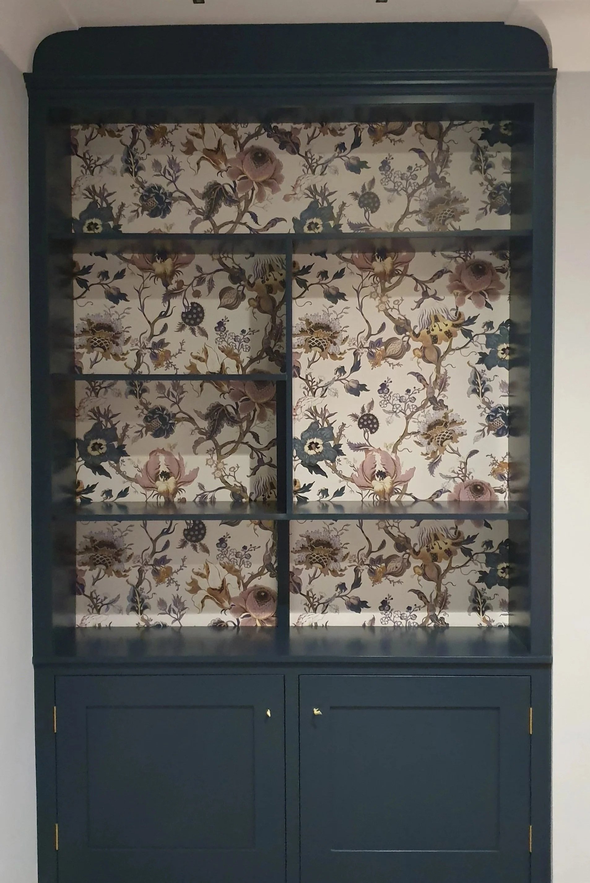 A dark blue display cabinet with glass doors and a decorative wallpaper background featuring floral and bird patterns.