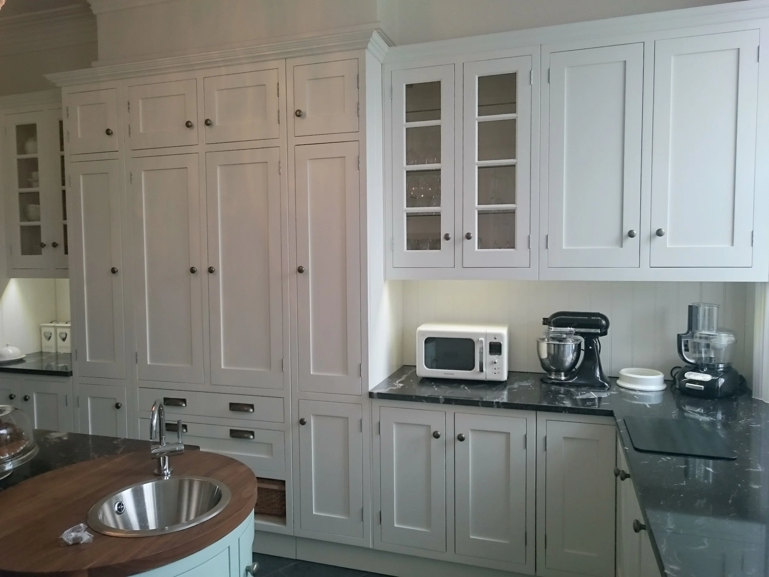 Large traditional painted kitchen units with tall storage cupboards, wicker baskets and black granite worktops 