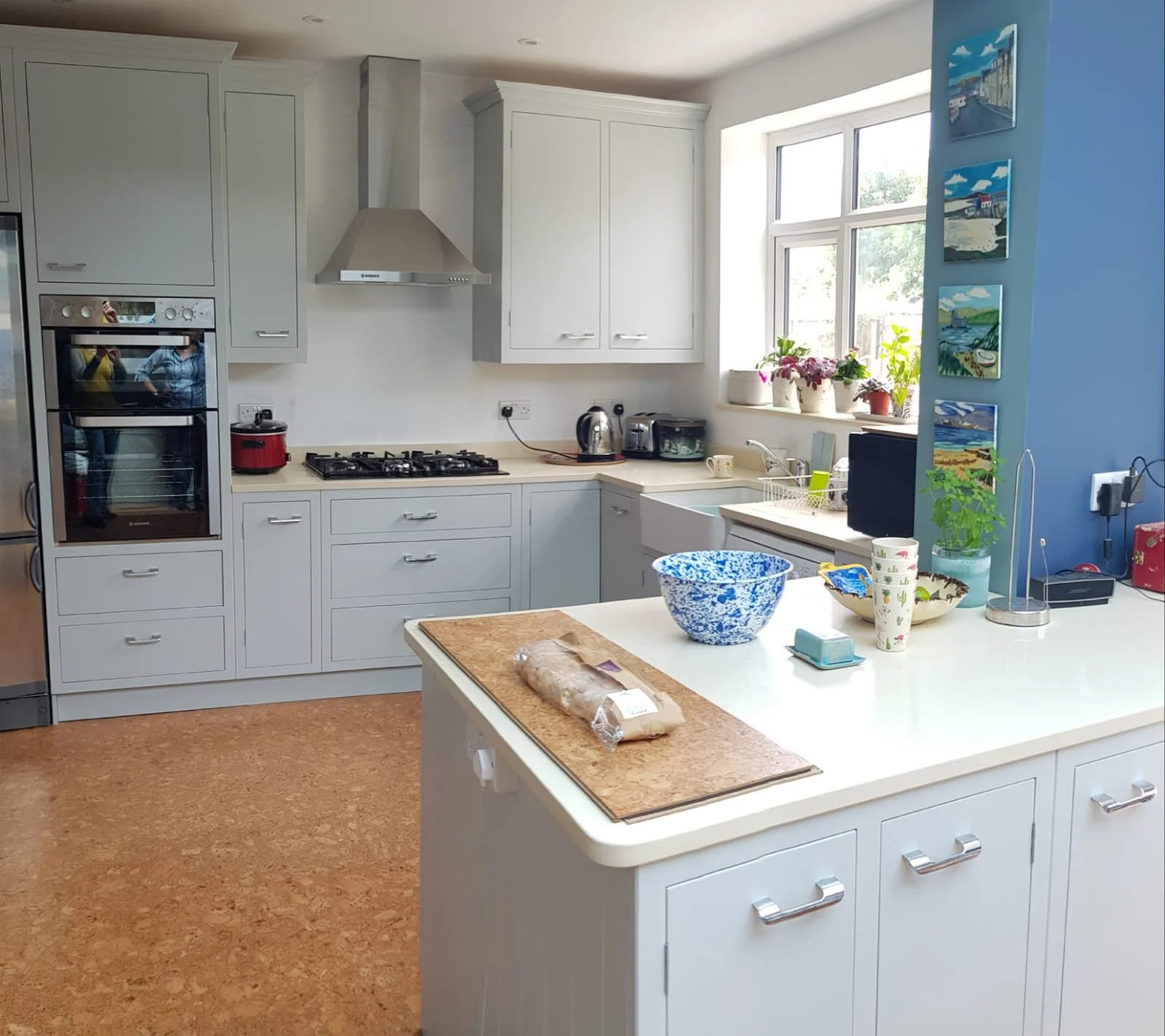 Modern kitchen with white cabinets, a window with potted plants, and an island with a blue bread bowl and various kitchen items.