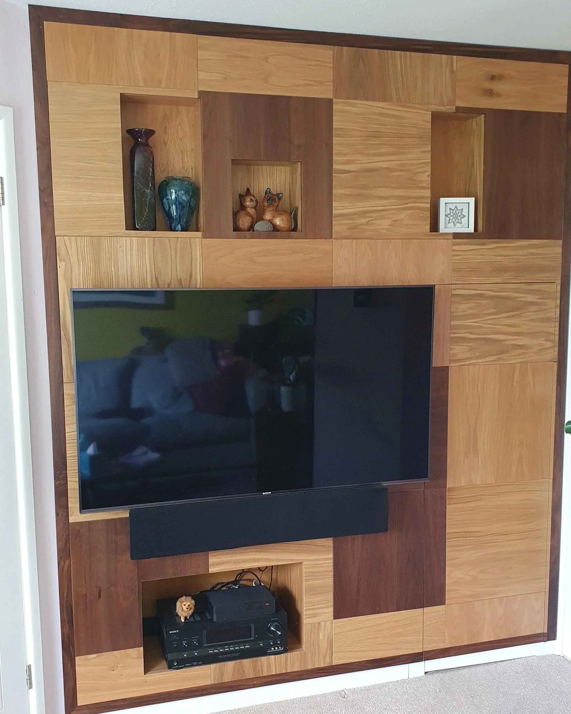 Wooden entertainment unit with a large flat-screen TV, decorative vases, and small animal figurines on open shelves.