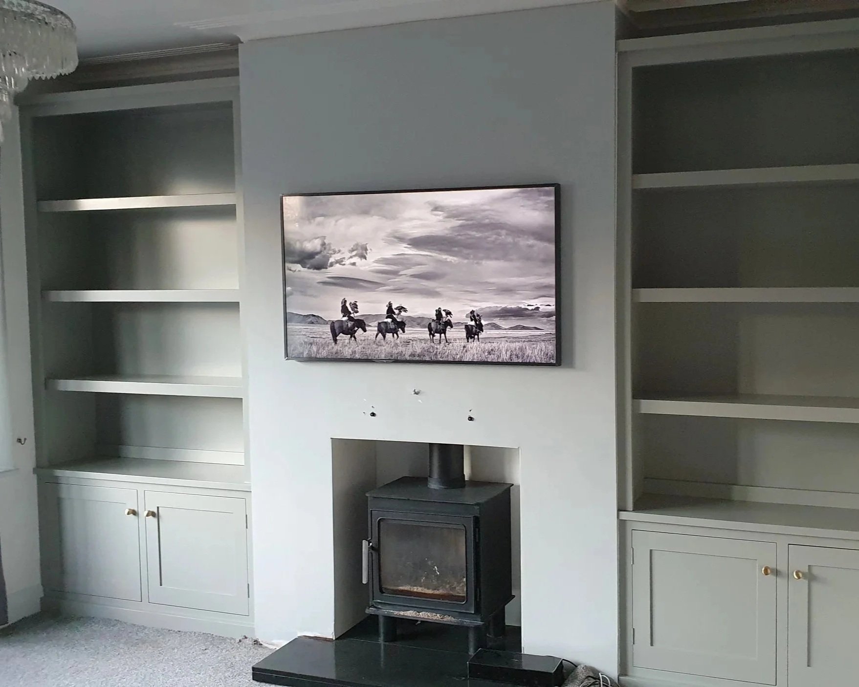 A living room with a wall-mounted flat-screen TV on a chimney breast. With built in alcove bookshelves on either side.