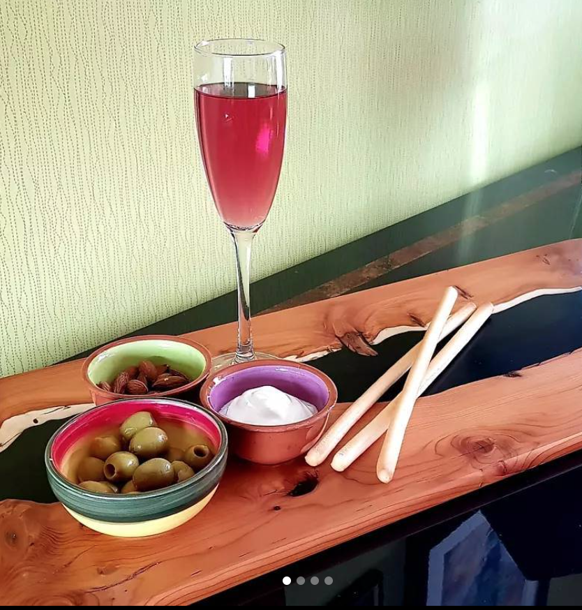 A glass of red wine, bowls of green olives, black olives, and sour cream, along with three breadsticks on a wooden serving board.
