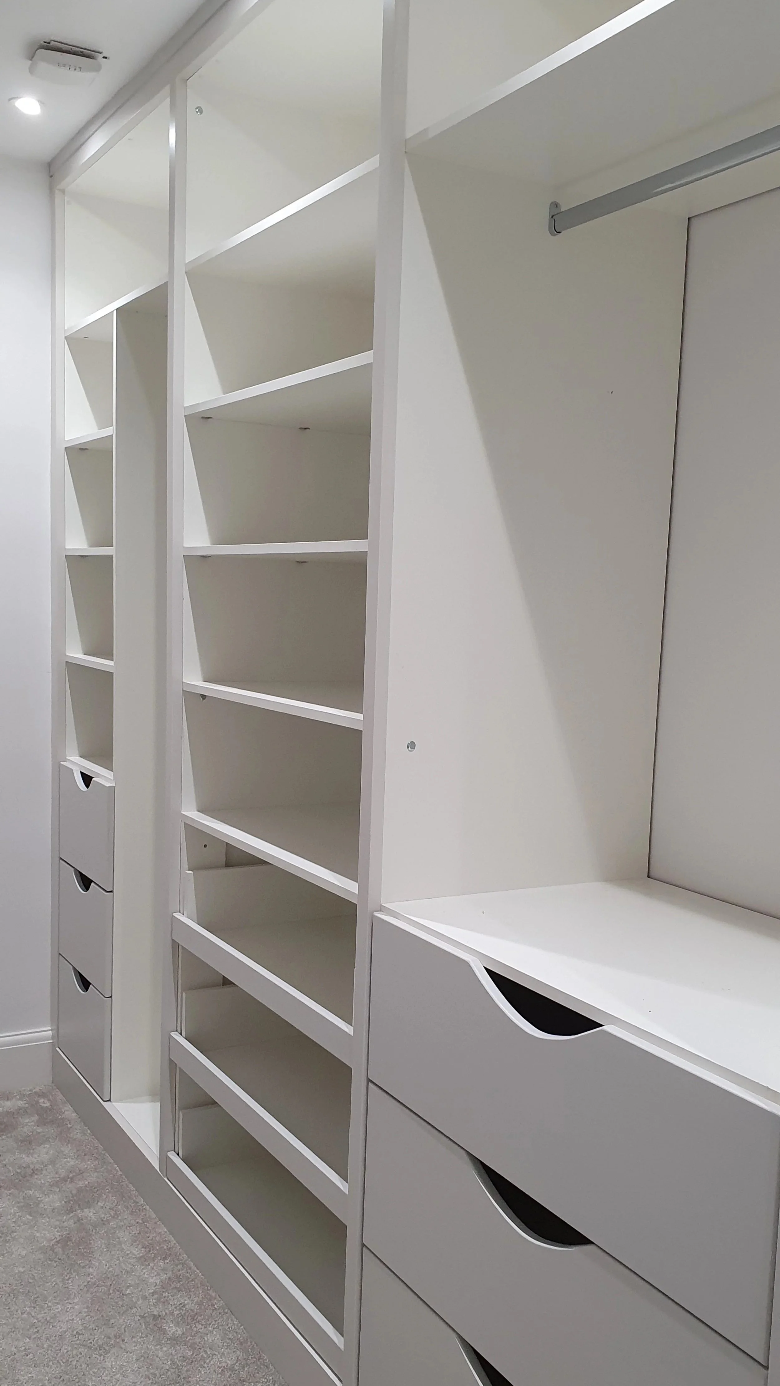 Empty white shelving unit with drawers and open shelves in a room.