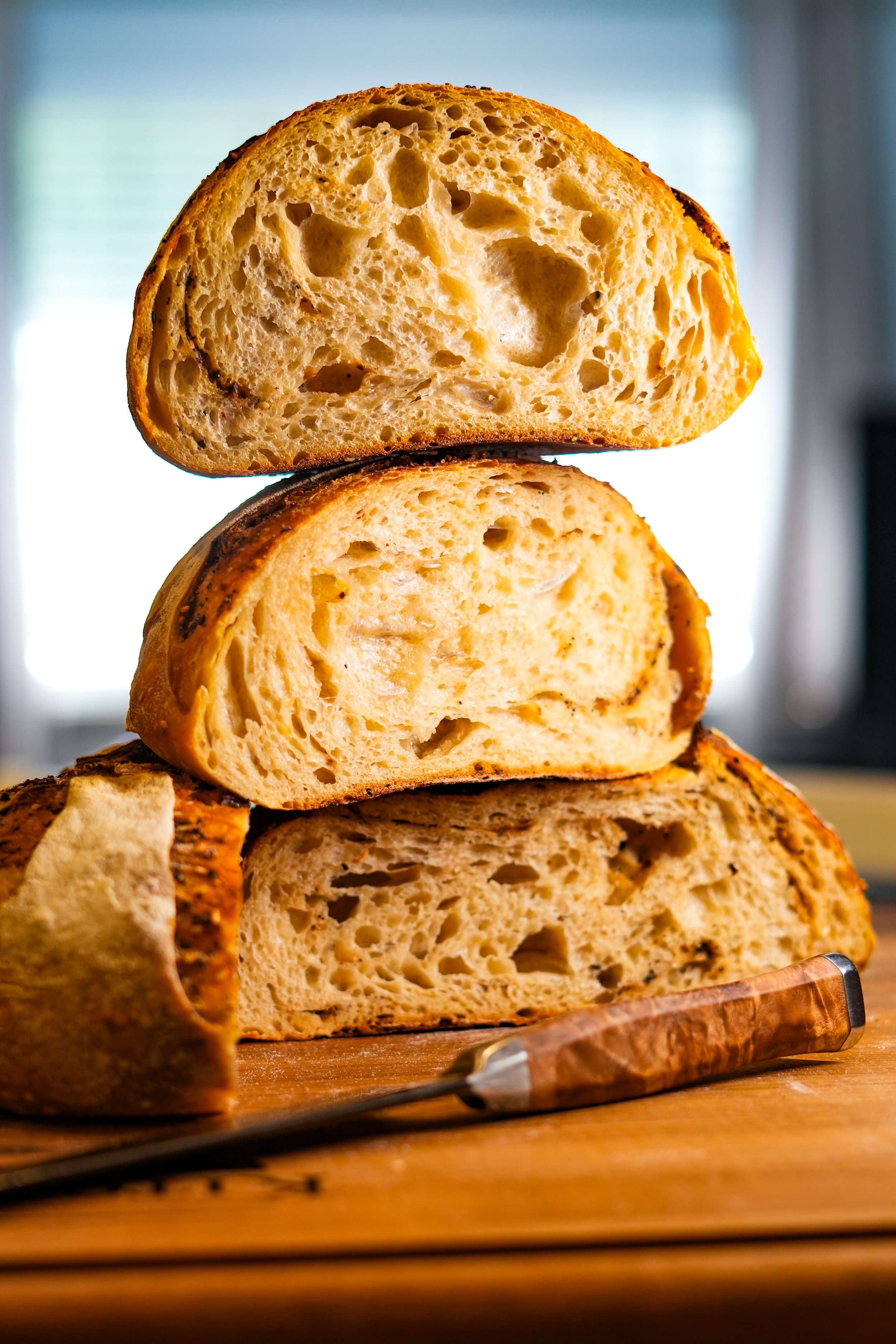 Close-up of a sliced loaf of rustic bread with a knife on a wooden cutting board.