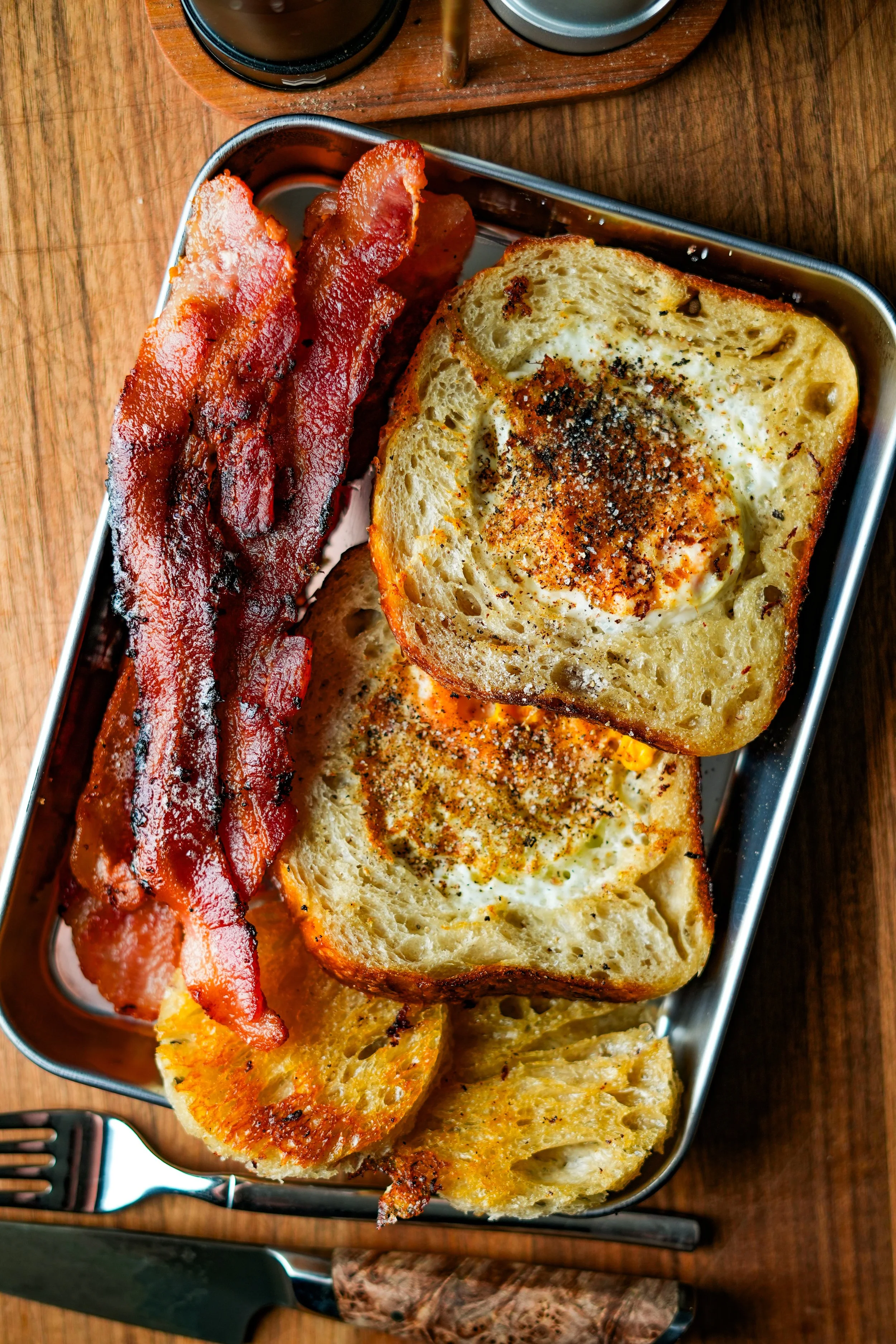 Bacon, toasted bread with eggs, and hash browns served on a metal tray.