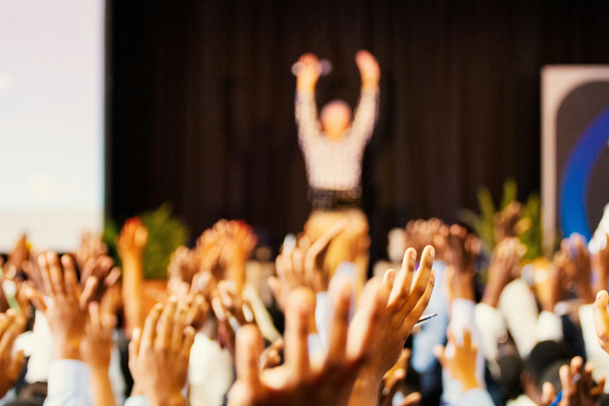 A large group of people raising their hands towards a speaker on stage at a conference or event.