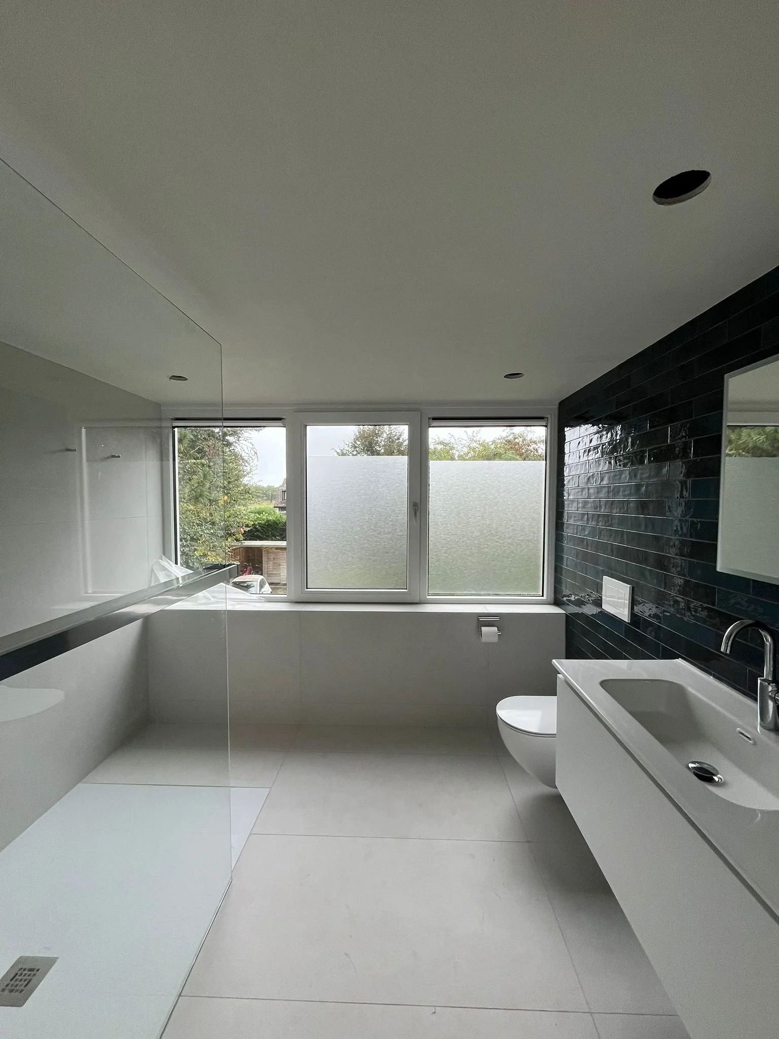 Moderne badkamer met grote ramen, zwarte tegelmuur, wit wastafel en toilet, in een minimalistische stijl