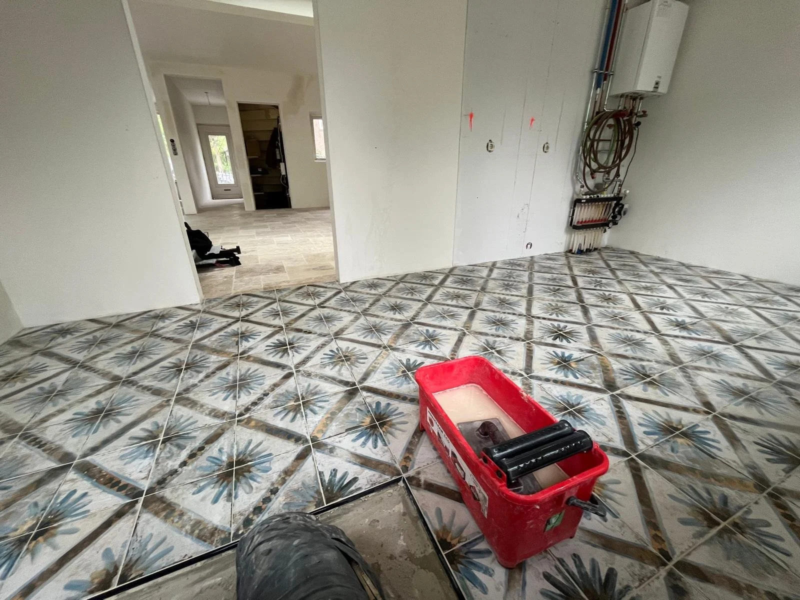 Binnenruimte van een huis dat wordt gerenoveerd, met kleurrijke betegelde vloer en bouwgereedschap, muren zonder afwerking en elektrische installatie zichtbaar.