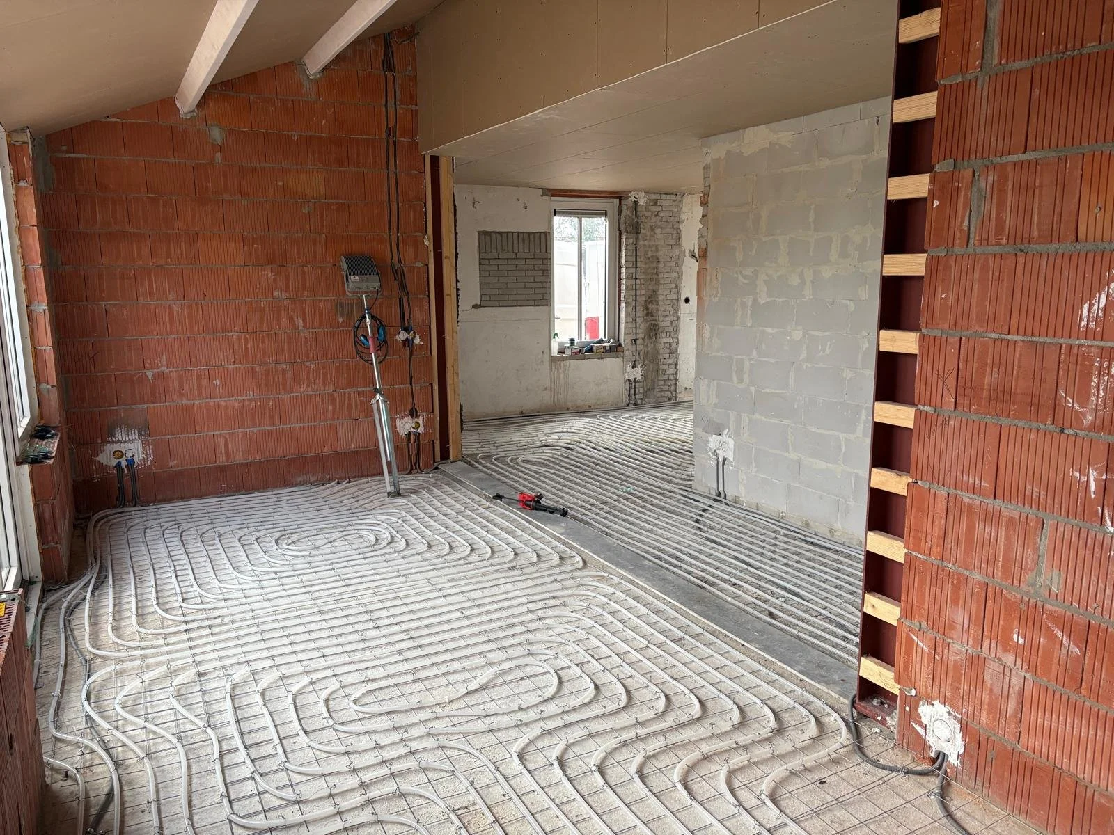 Binnen in een bouwplaats met zichtbaar verwarmingsmantel en leidingwerk op de vloer in een kamer met bakstenen muren en een klein raam.